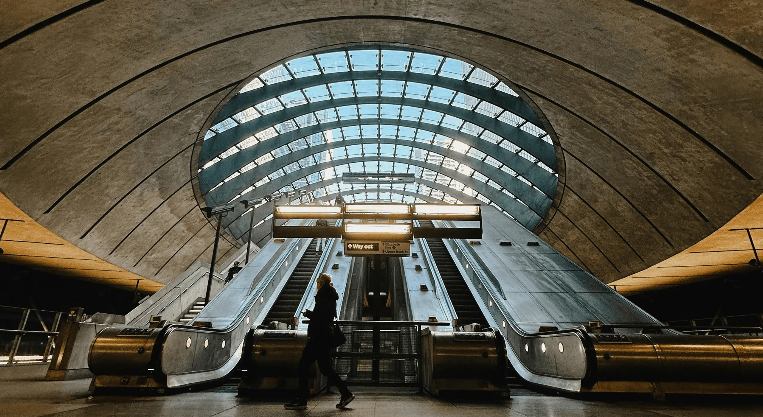 Person walking past escalators under a vaulted glass ceiling.
