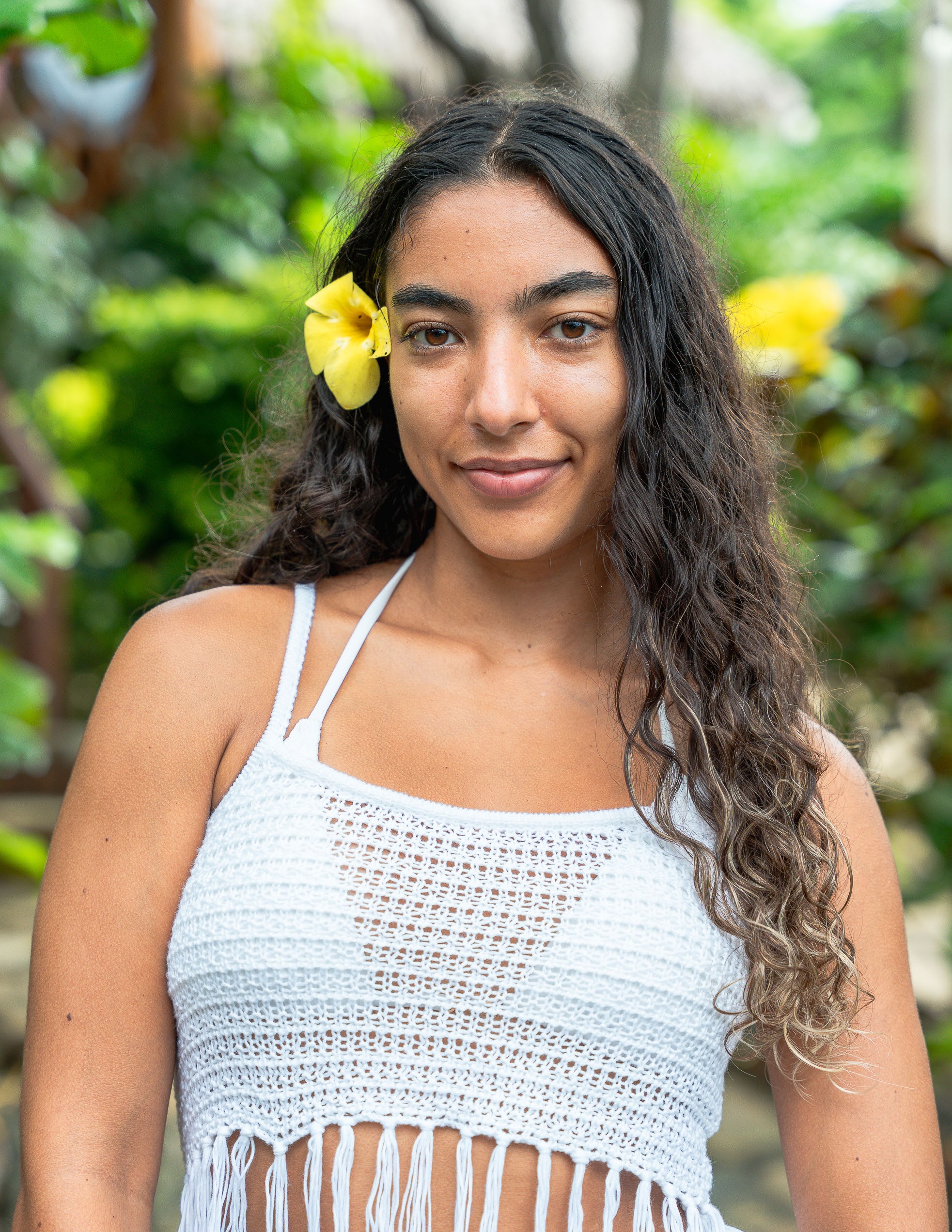 Smiling woman in beige linen outfit standing indoors with plants and books in the background.