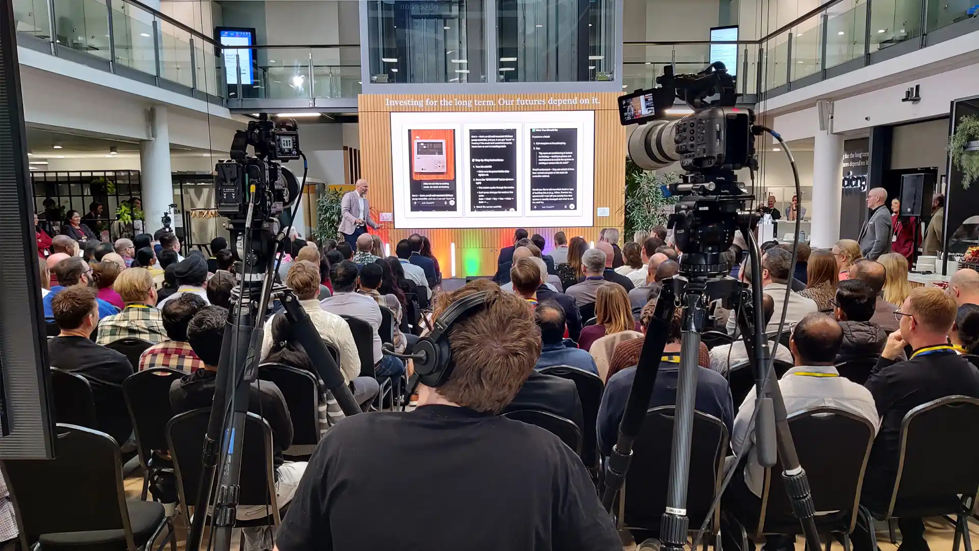 Wide shot of the plenary session at the L&G Retail Tech Summit, showing live cameras, stage screens and seated audience.
