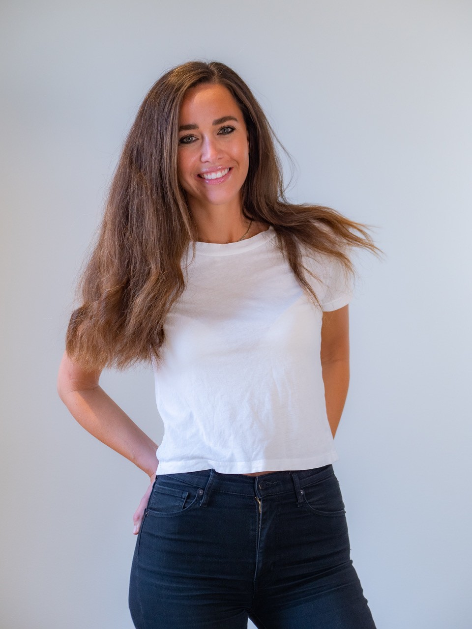Close-up portrait of a blonde woman in translucent pink glasses and a white shirt on a soft blue background.