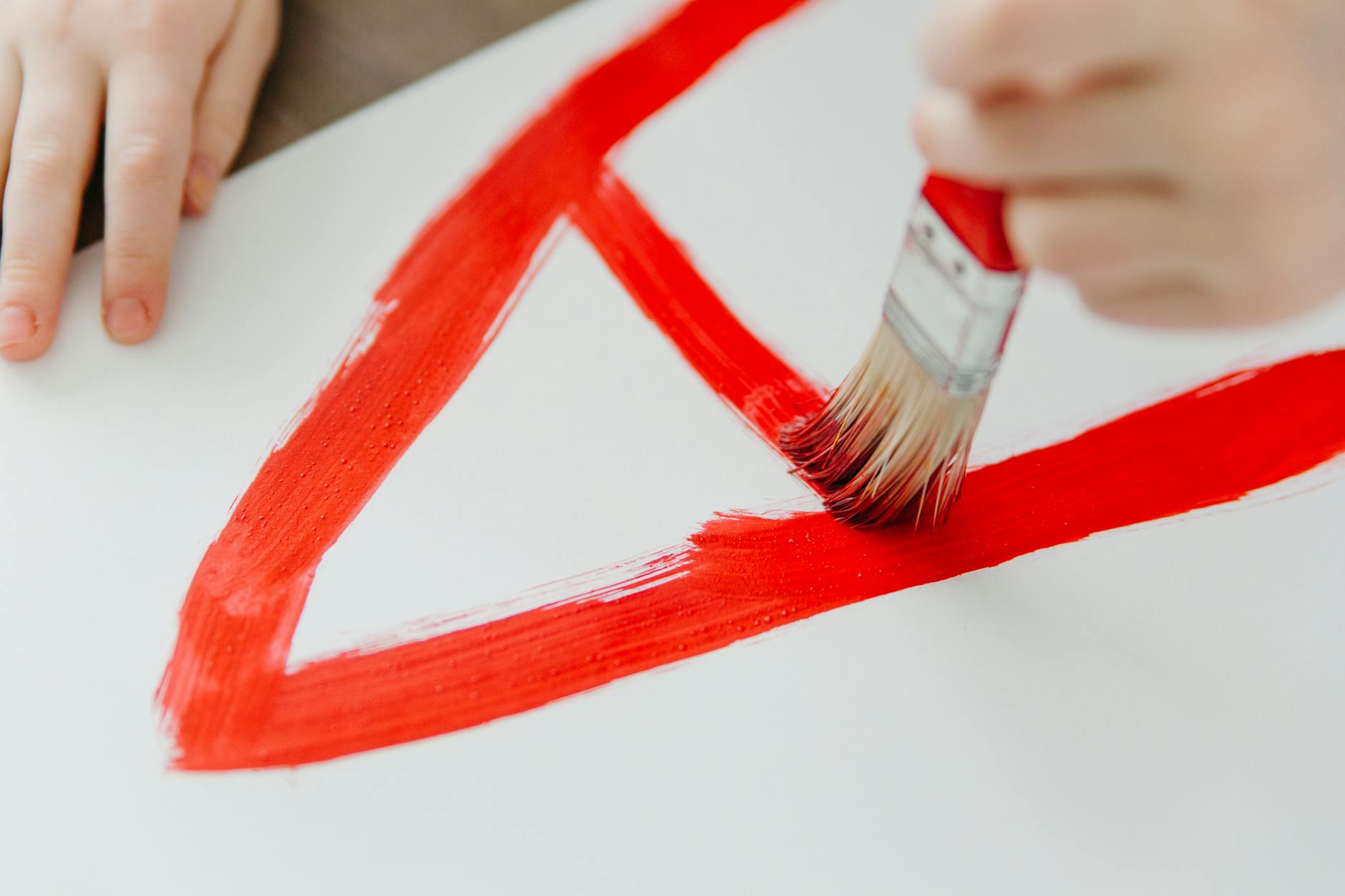 A tabletop covered in glue sticks, safety scissors, and bright construction paper cut into various polygons.