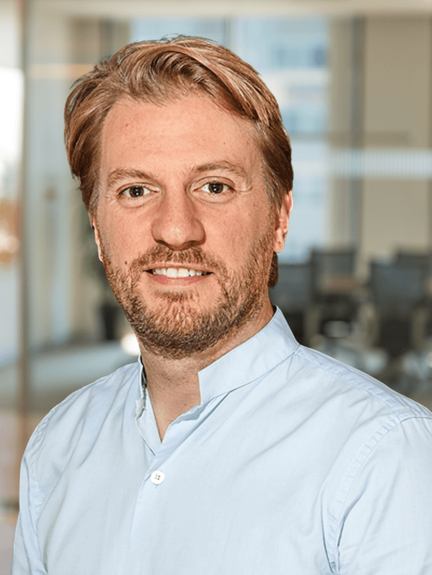 Smiling person with curly hair, wearing a black shirt, against a warm, dark background.