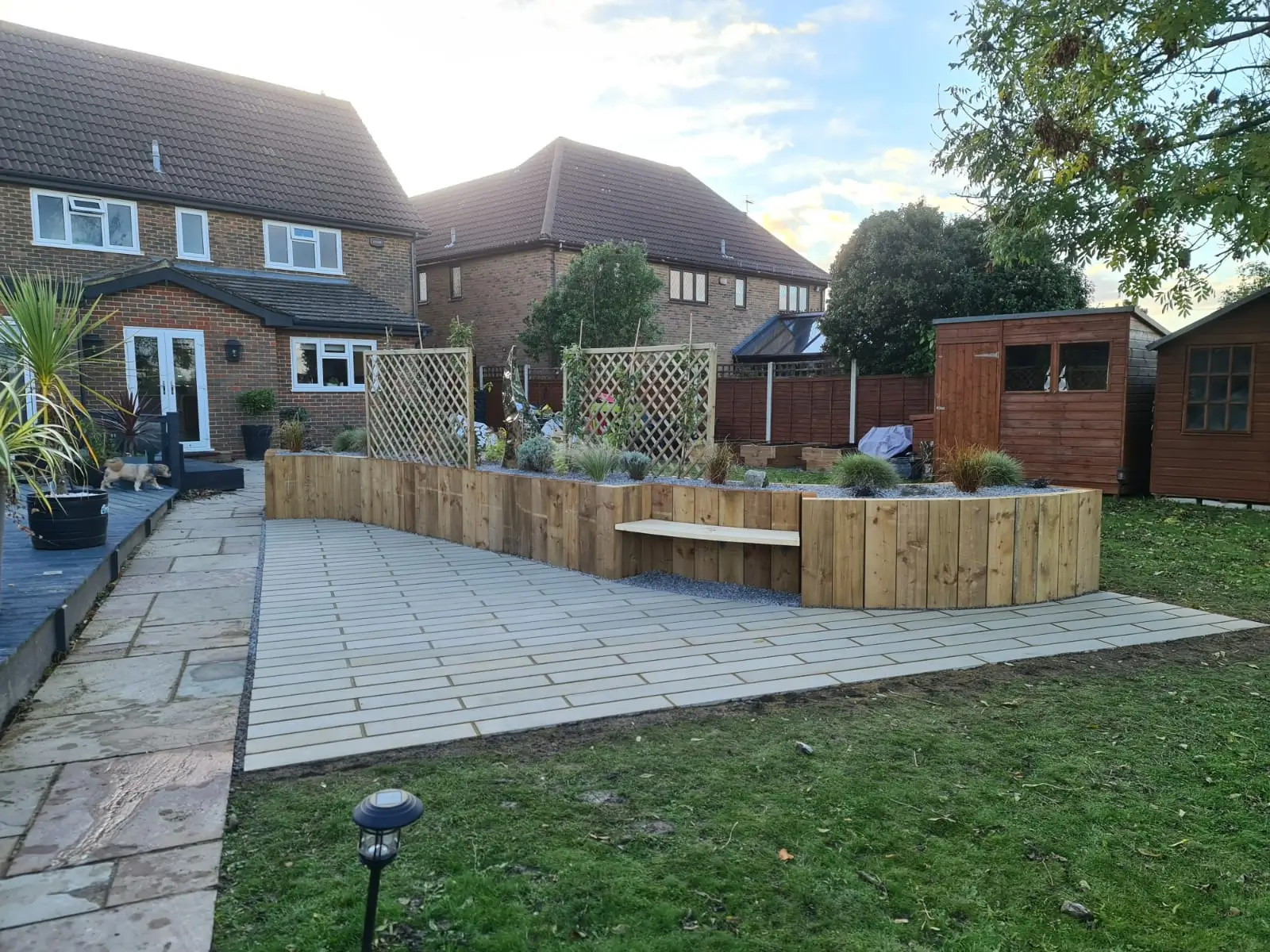 A well-maintained garden with a patio, seating area, greenery, and a few wooden structures.