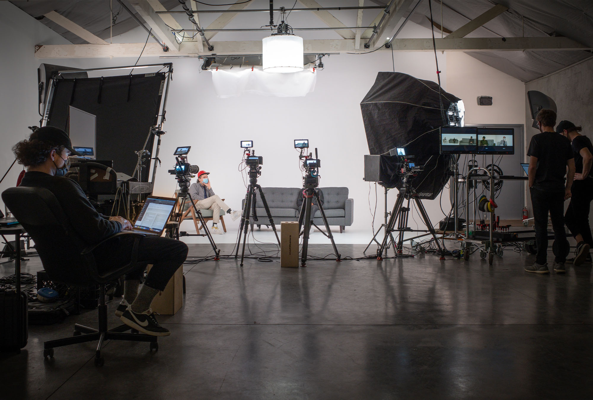 A photo of the soundstage at Particle Studio in seattle. There are three cameras set up for an interview with Amazon's DEI team. A teleprompter and operater sit ready to operate their machine. The DP and Grip review monitors in the corner to ensure the image is good to shoot.