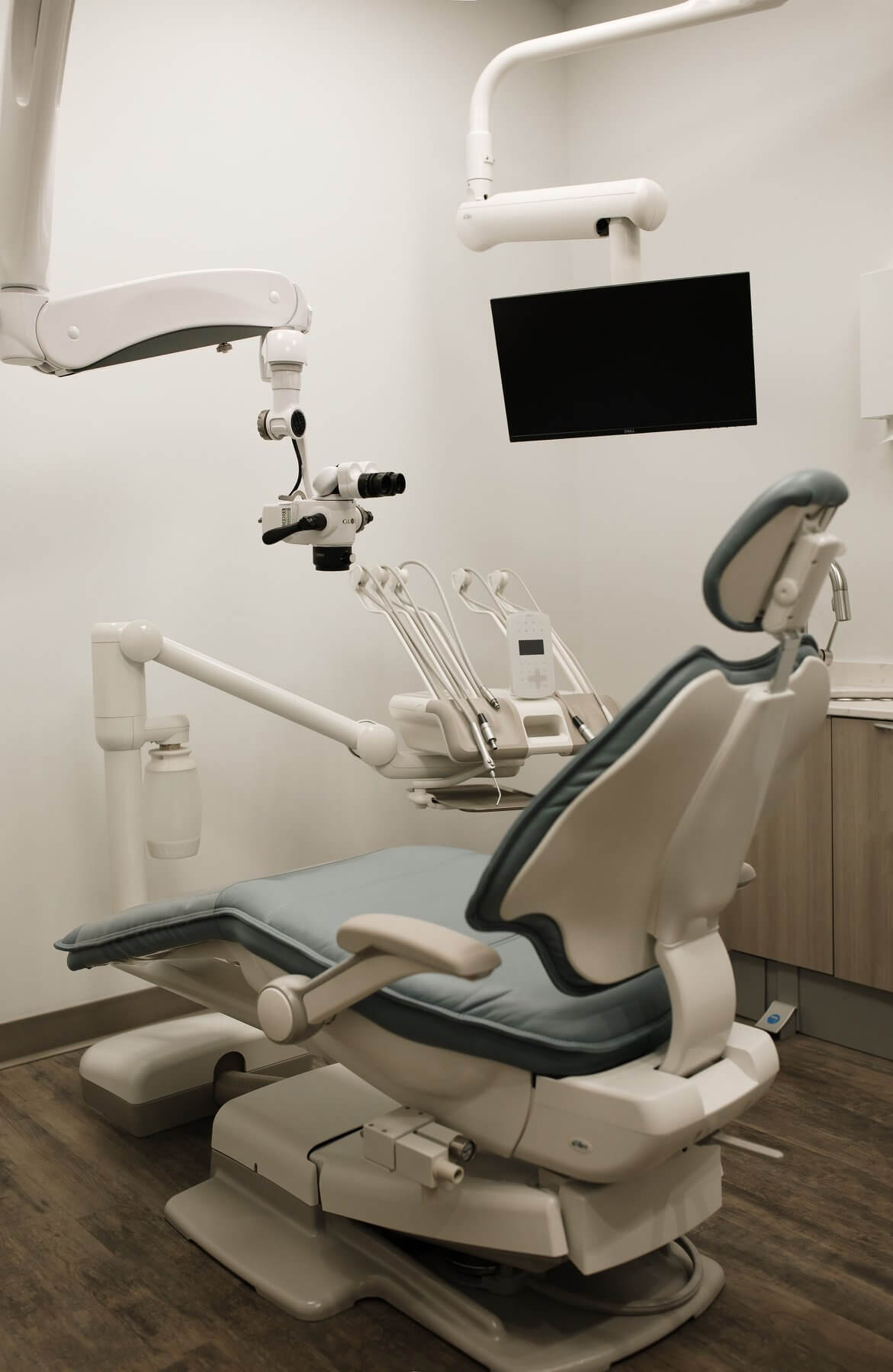 A dental clinic interior featuring a patient chair, dental equipment, and a wall-mounted screen.