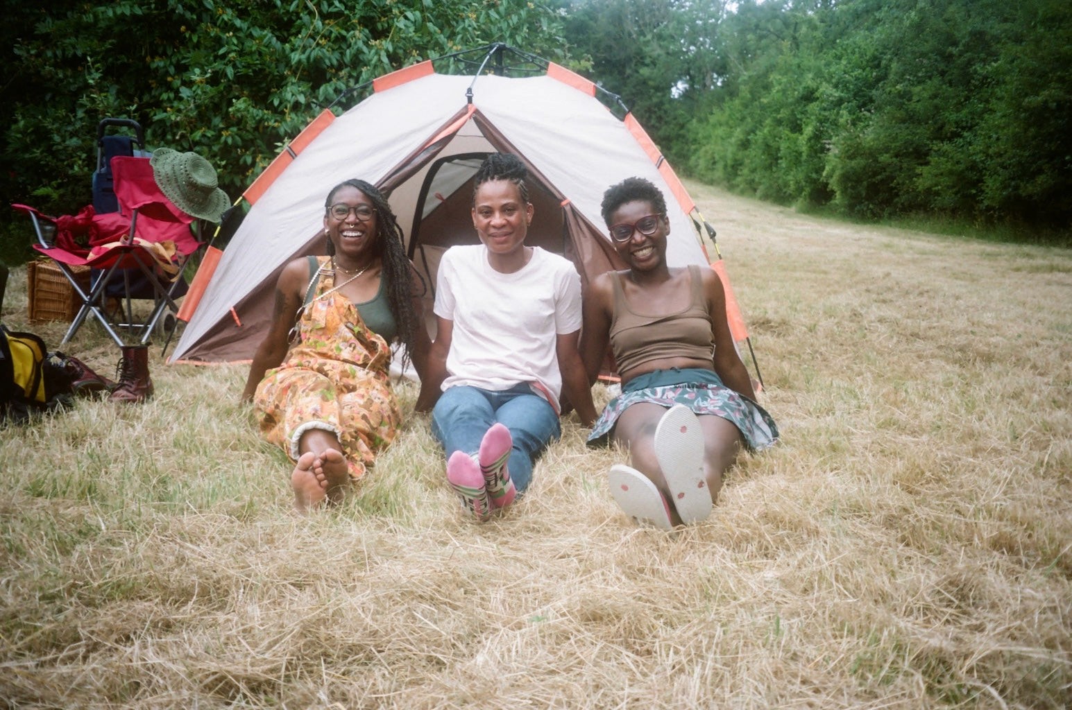 A few people sit and lie on the grass in the sun, near a festival tent
