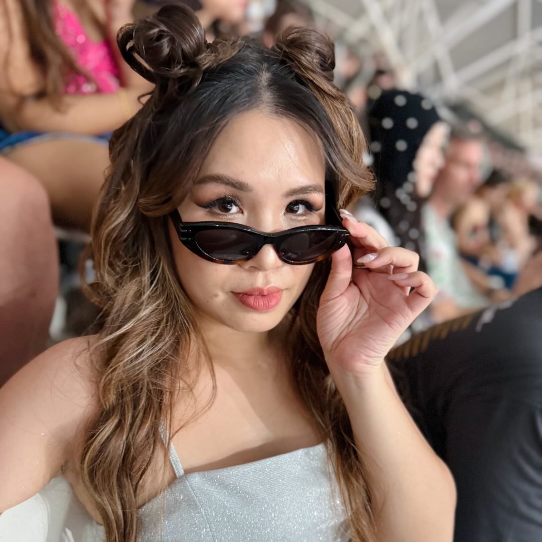 Close-up portrait of a freckled woman with soft pink hair and star earring, natural light, white tank top.