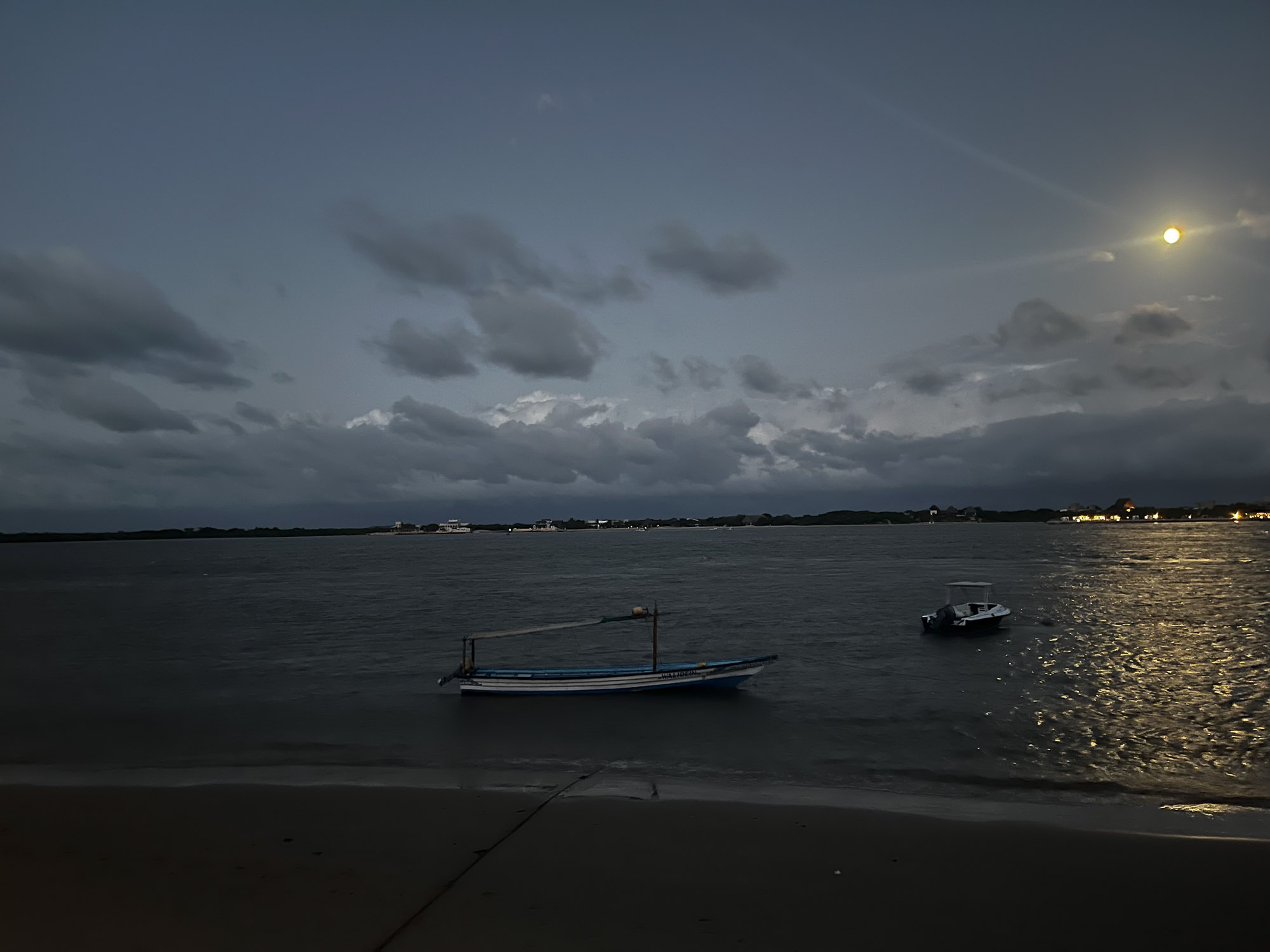View of beach with boats on the water in the evening.