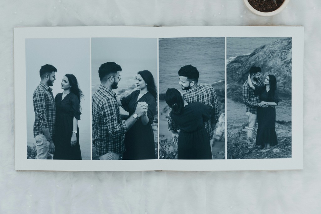 A photo album open to a page displaying a series of black-and-white images of a couple. The couple is seen in various affectionate poses near a rocky coastline, highlighting their romantic connection and the serene beauty of the natural backdrop. The layout captures intimate moments and the timeless essence of their relationship.