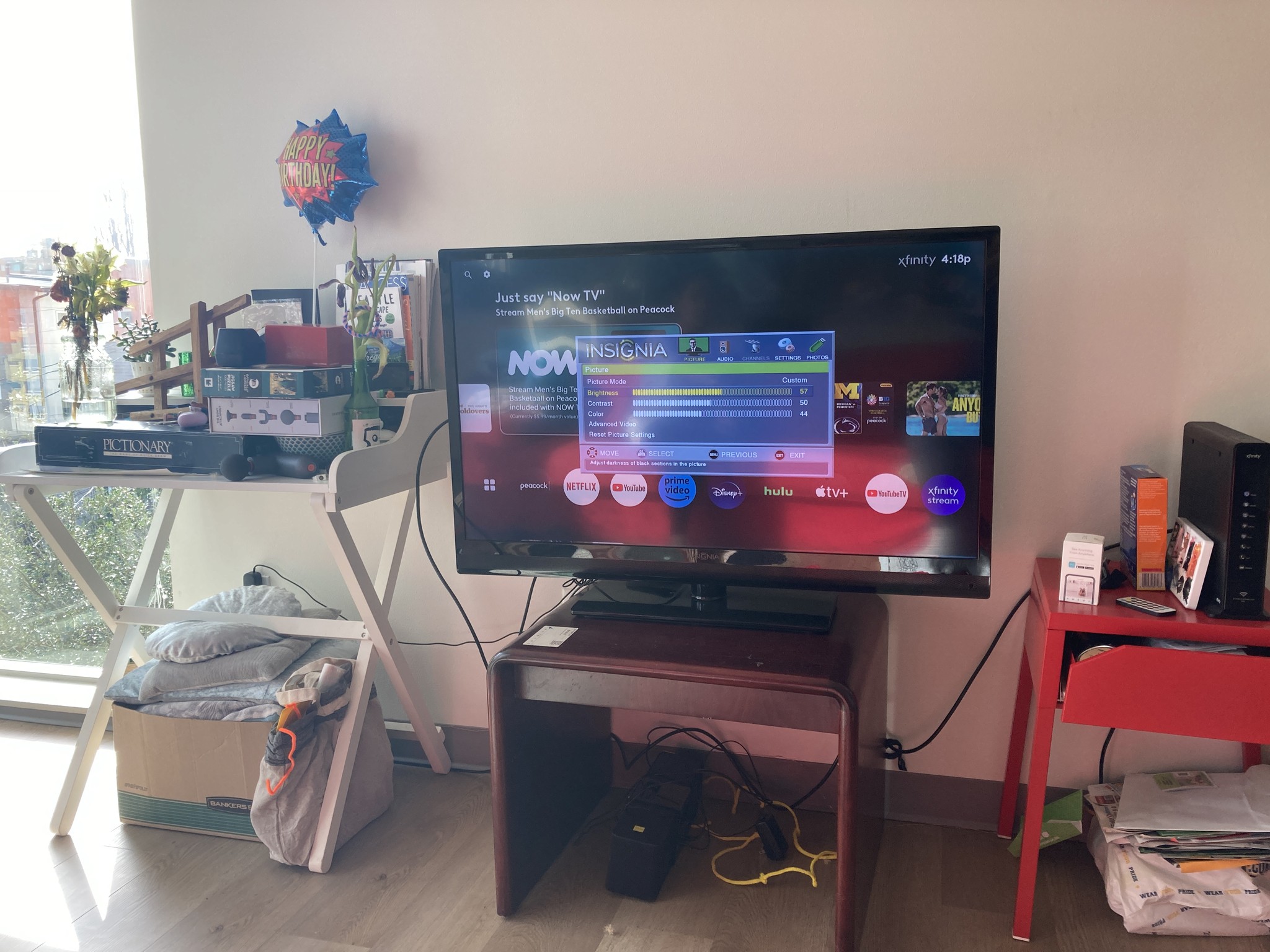 A TV mounted on a stand between two messy tables, with wires coming from all directions.