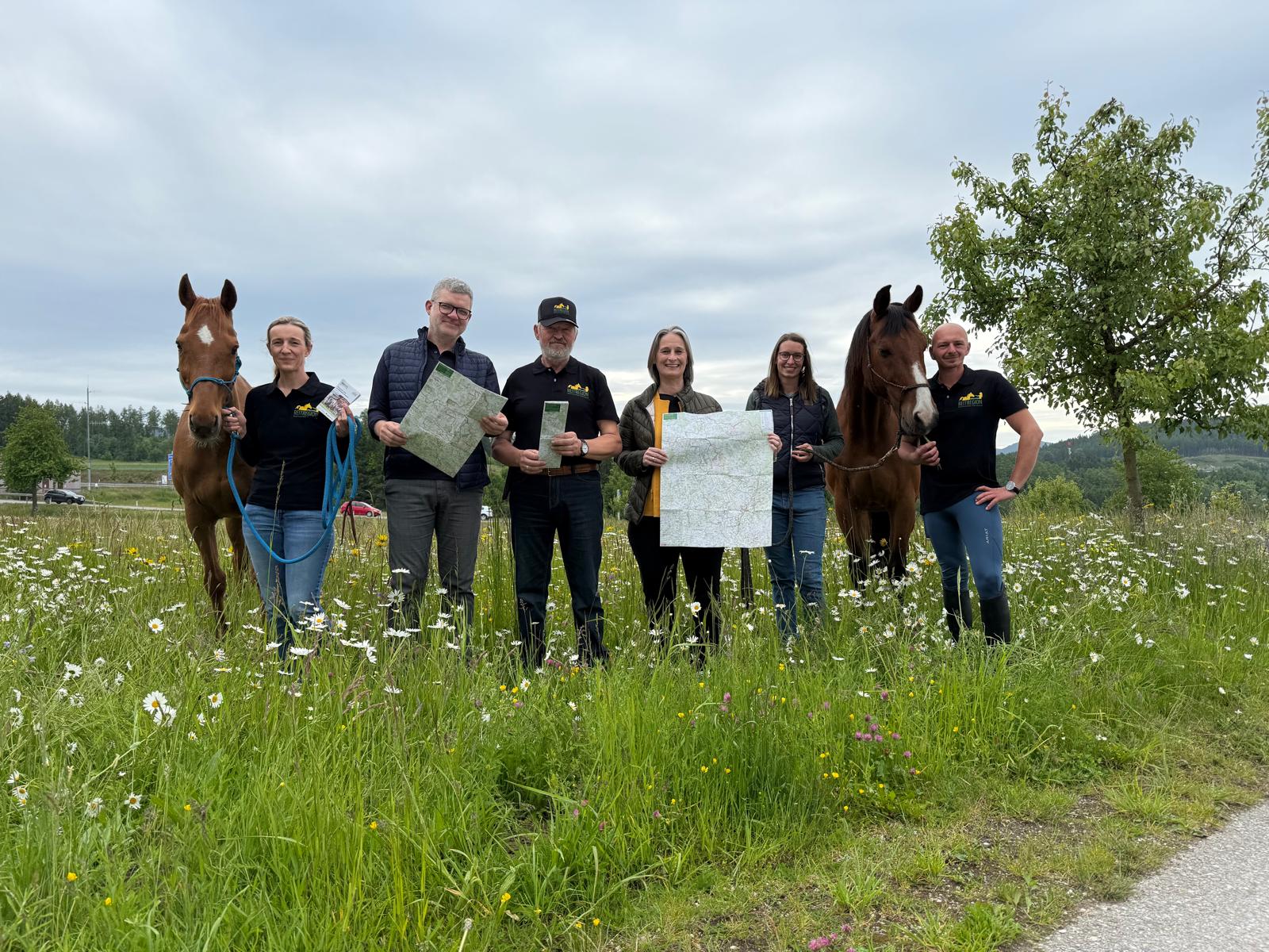 A smiling woman with her arms crossed, standing against a dark green background. She has long, dark hair.