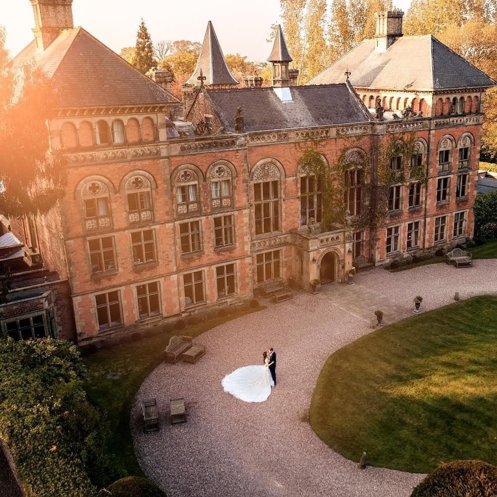 An elegant wedding ceremony setup features a domed gazebo adorned with peach and pink floral arrangements and lush greenery. White chairs line the aisle.