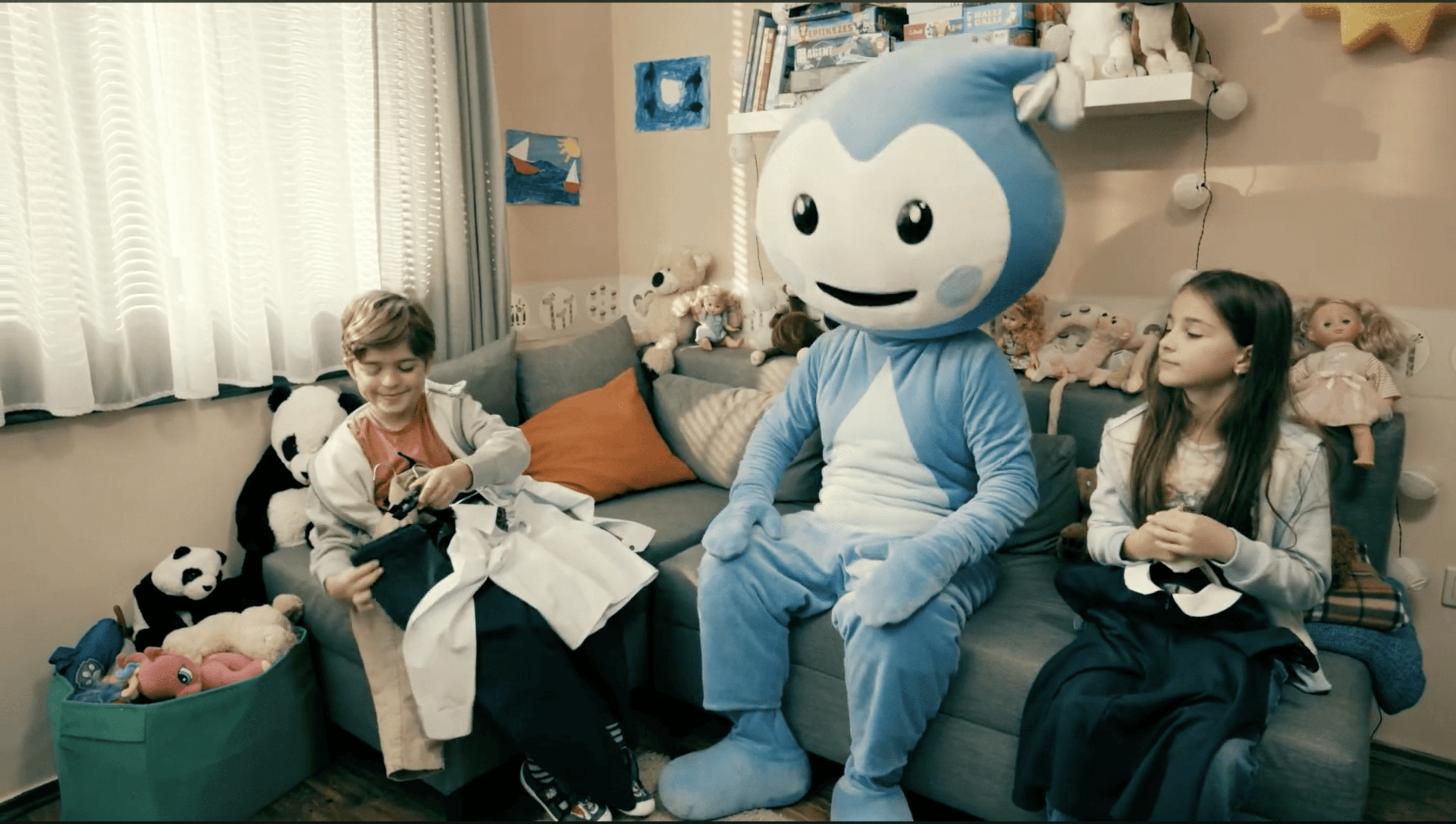 Cseppbarát kék kabalafigurája az ünneplőben ülő gyerekek között.