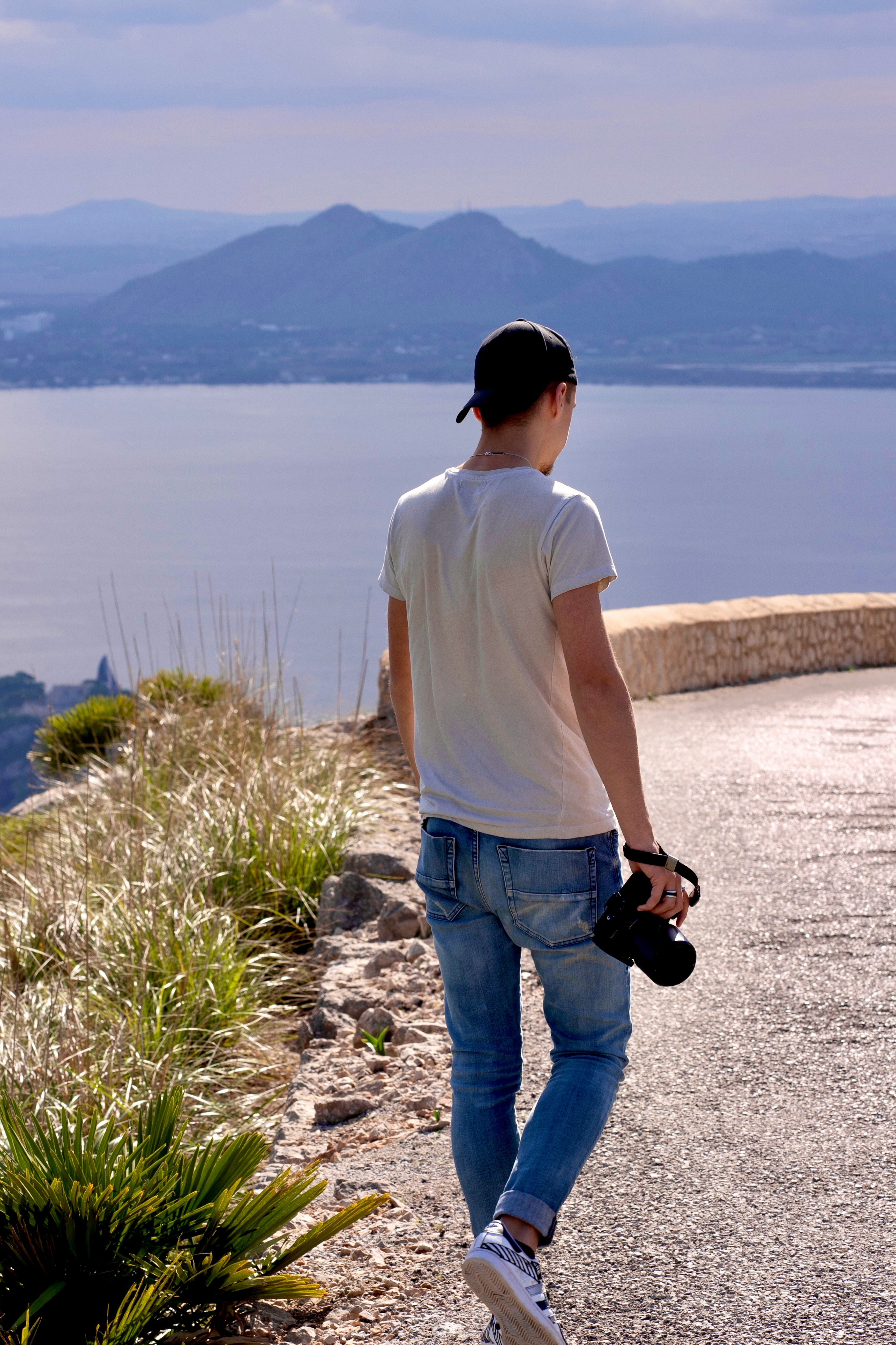 a man walking down a road next to a body of water