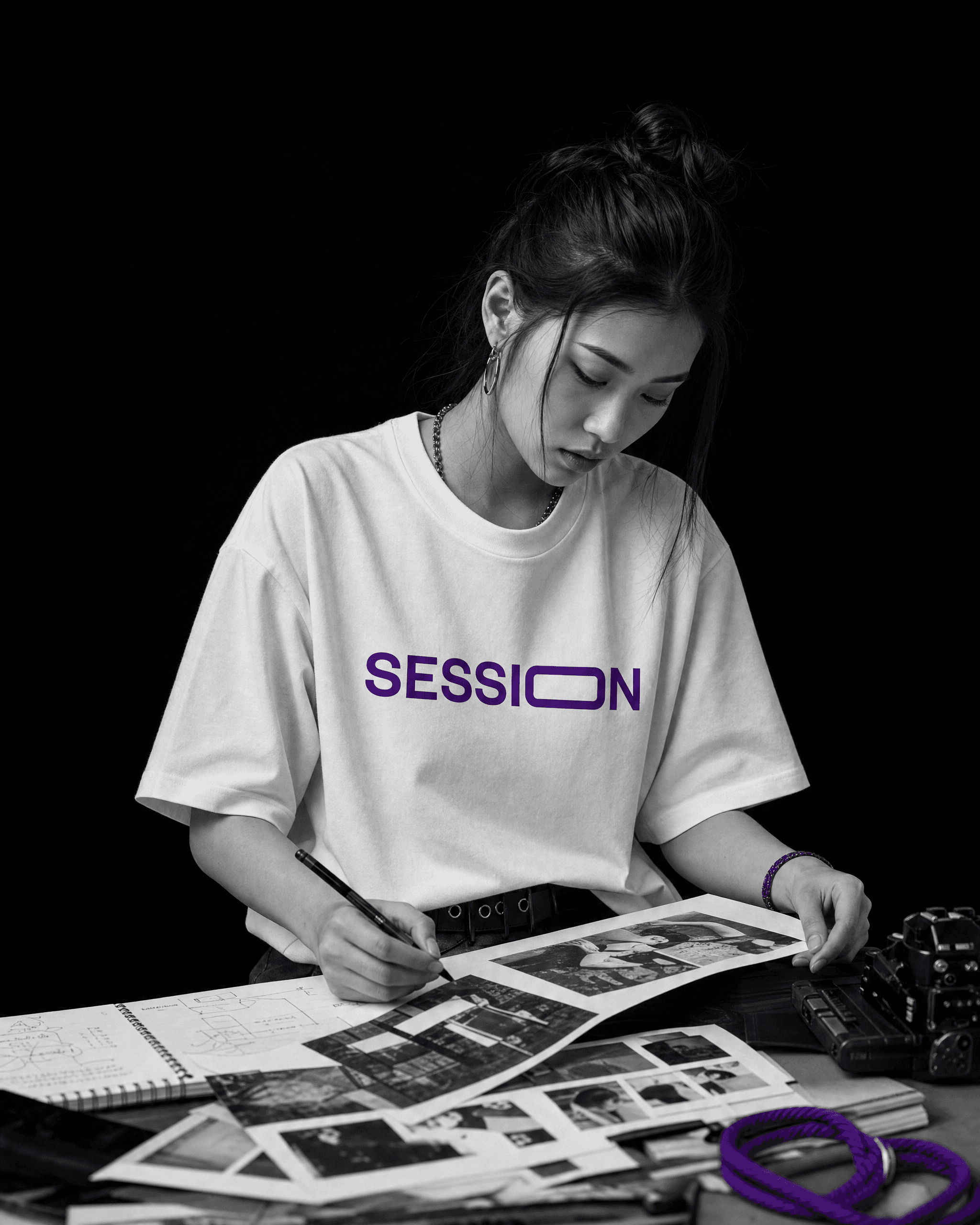 Woman in a white Session Zone purple-logo T-shirt reviewing photo contact sheets at a table.