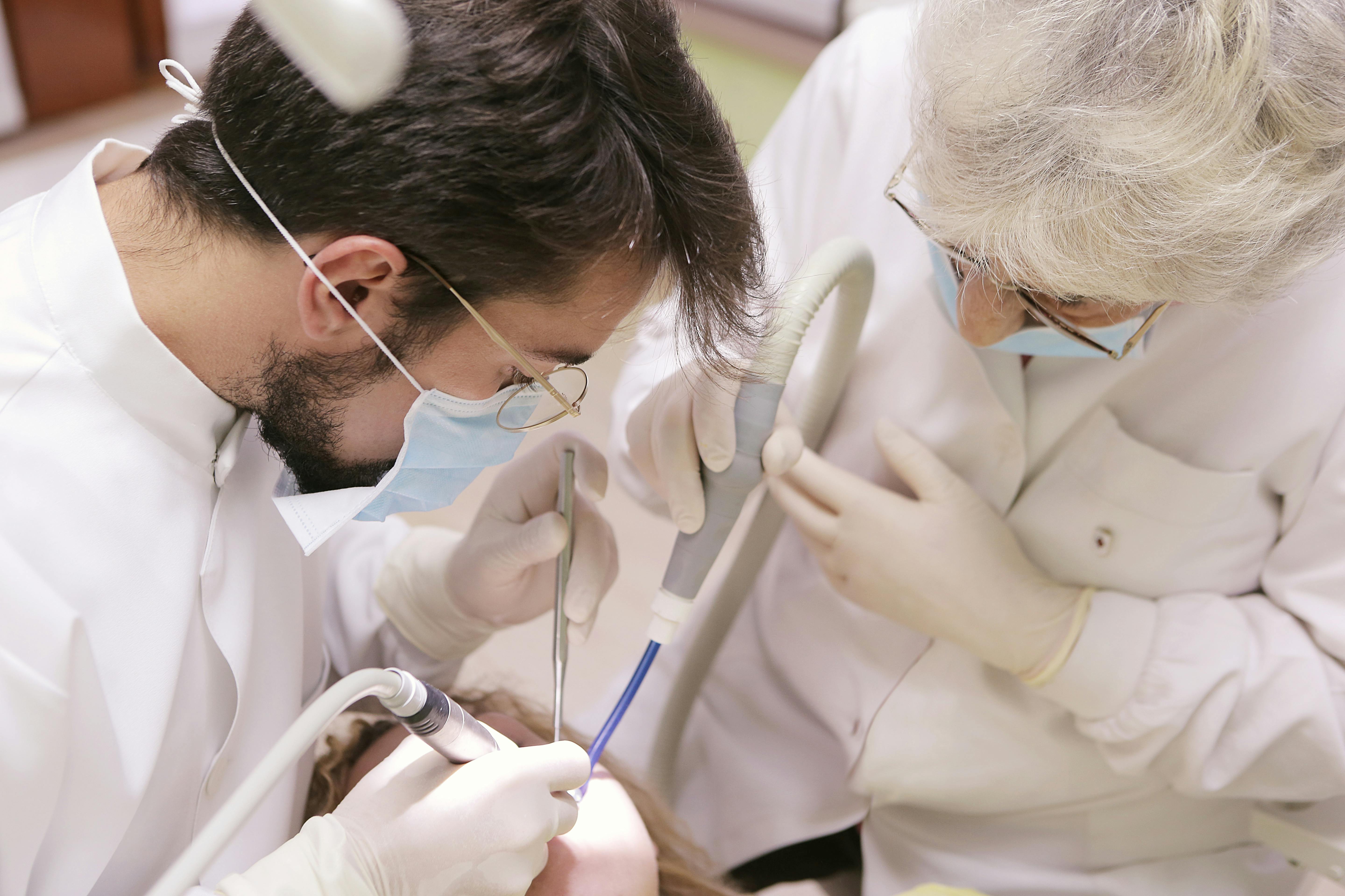 two dental professionals, one older and one younger, wokring on a patient