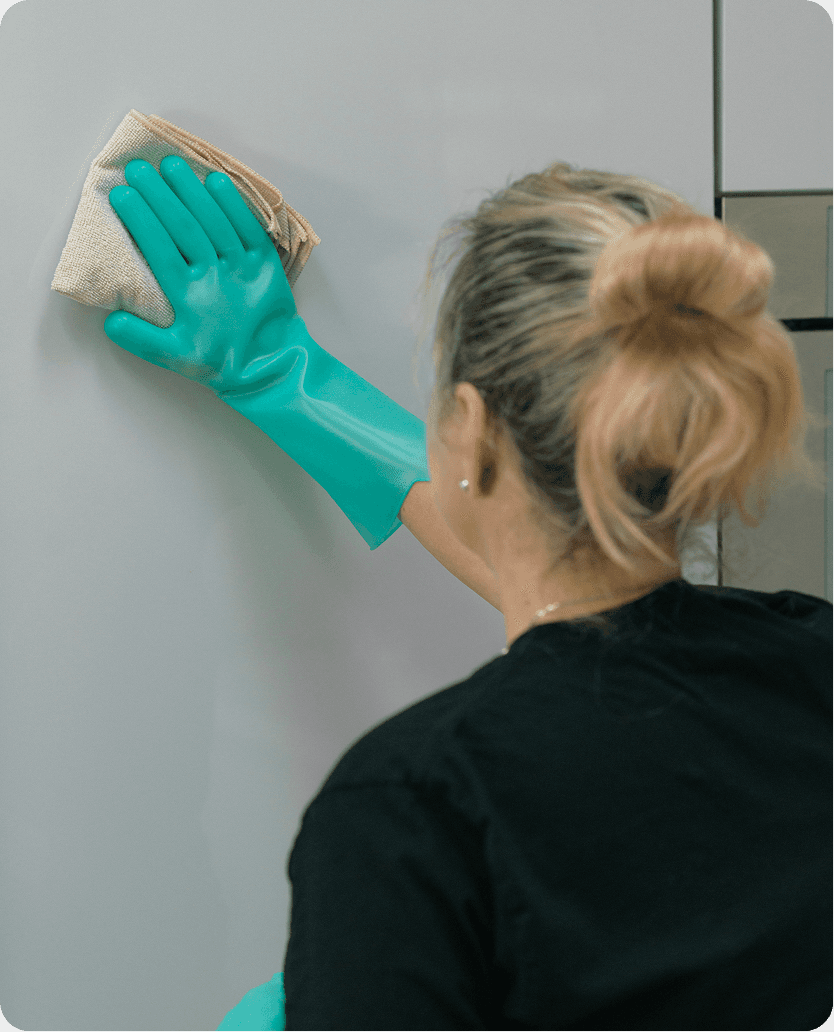 The cleaner is wiping the fridge with a cloth.