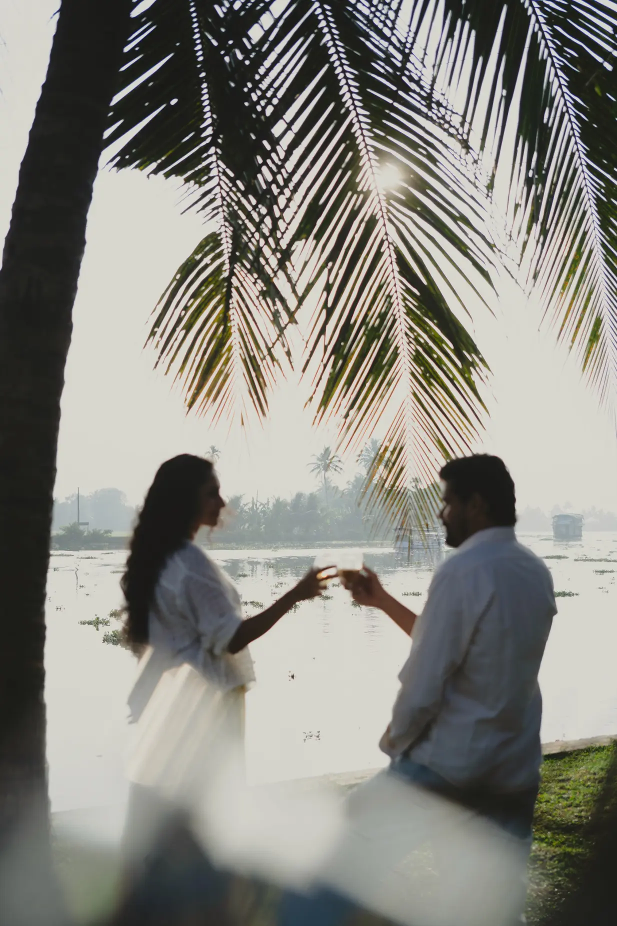 Bride and groom sharing a toast under a coconut palm by the Alleppey backwaters at sunrise