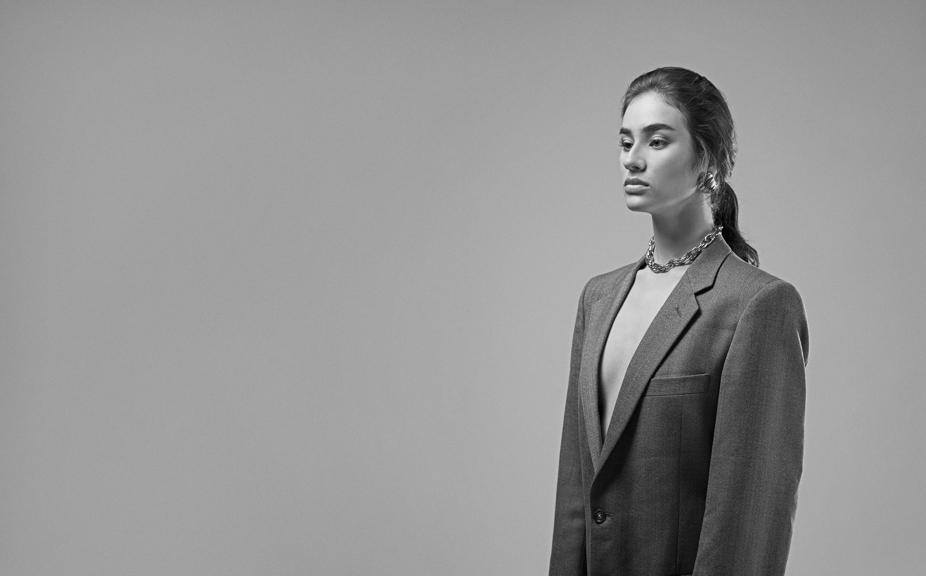 High-fashion studio portrait of a confident woman wearing an oversized blazer with a deep neckline, looking to the side with a strong, self-assured attitude.