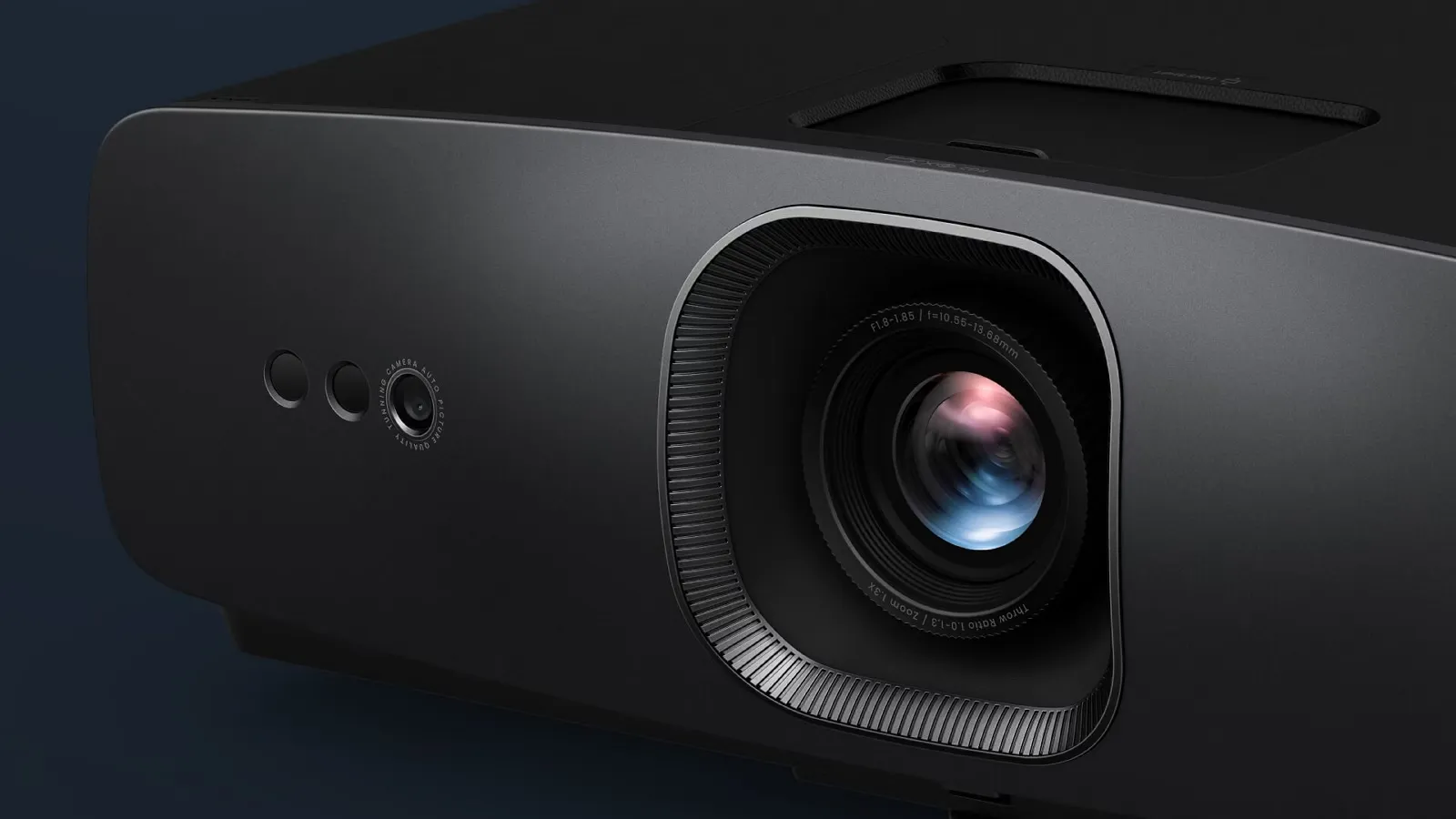 A sleek, modern black projector with a prominent lens and reflective glass surface is positioned against a dark, minimalist background, highlighting its advanced technology and design.