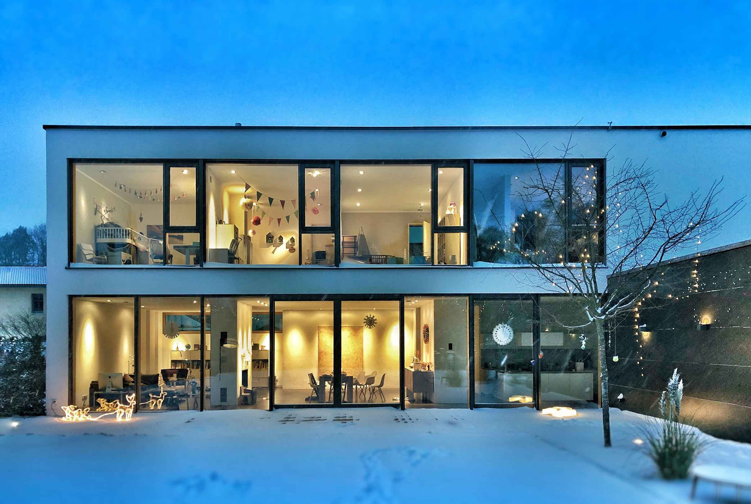 A warm looking home with lots of large glass windows on a snowy day