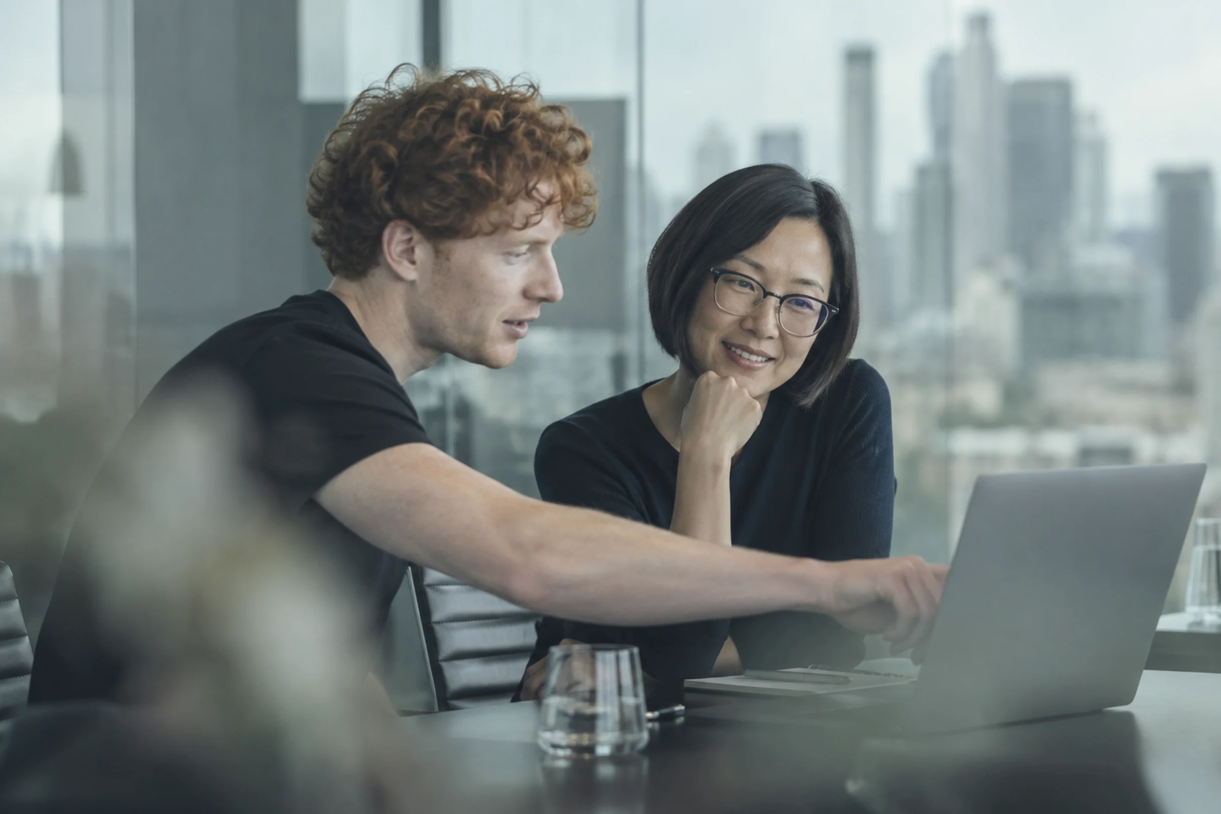 Two colleagues working at a laptop in a glass meeting room