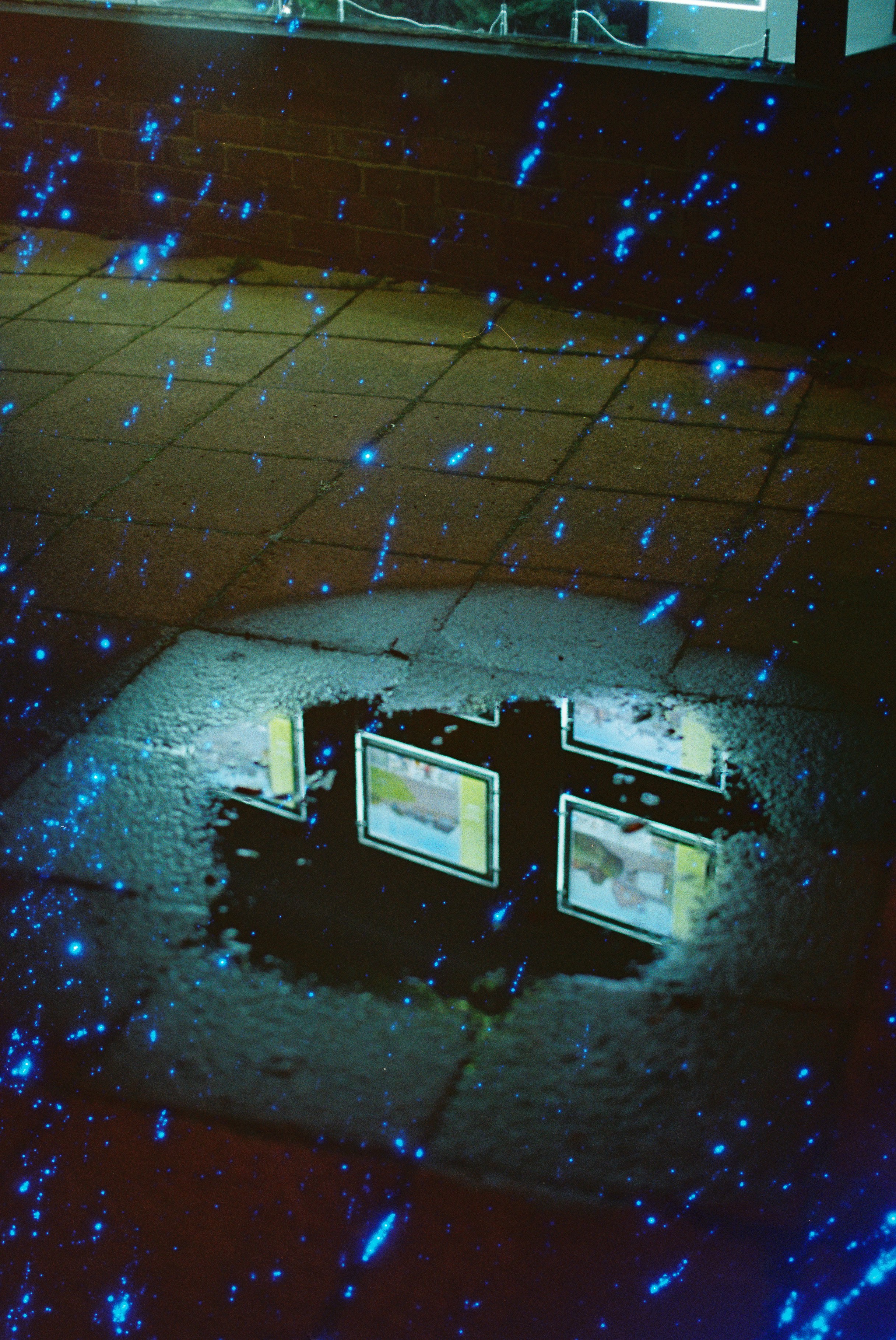 Puddle reflecting lights on a tiled surface at night.