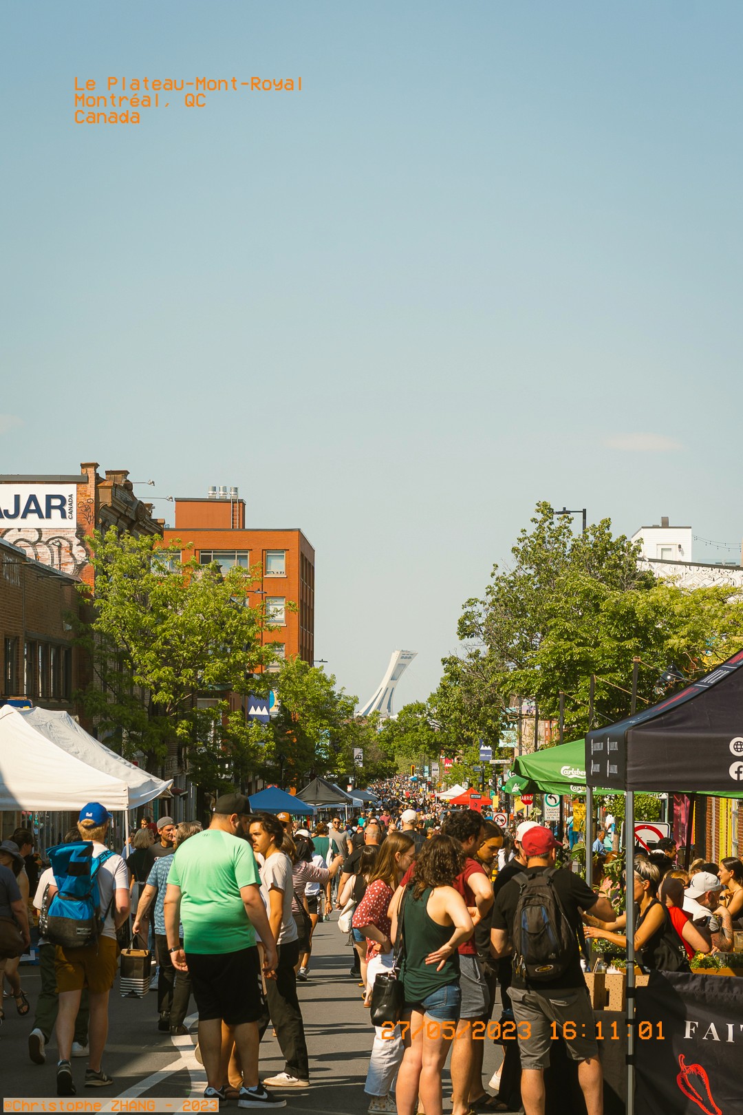 Rue bondée des passants sur Le Plateau-Mont-Royal avec la tour du Stade Olympique visible à l'horizon.