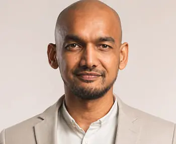 Bald man in a beige blazer posing against a neutral background