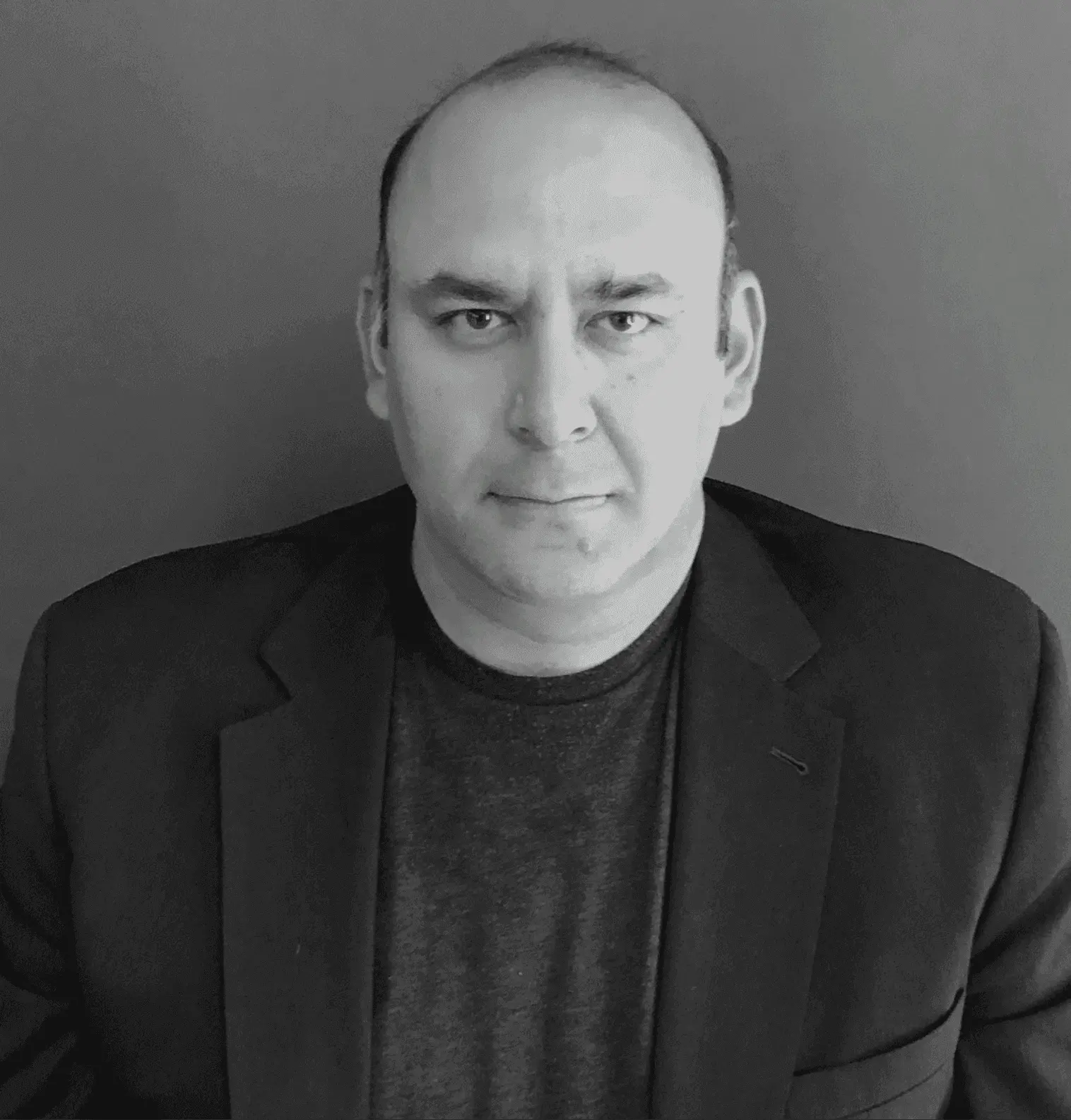 Man wearing a suit jacket and dark shirt, looking directly at the camera.