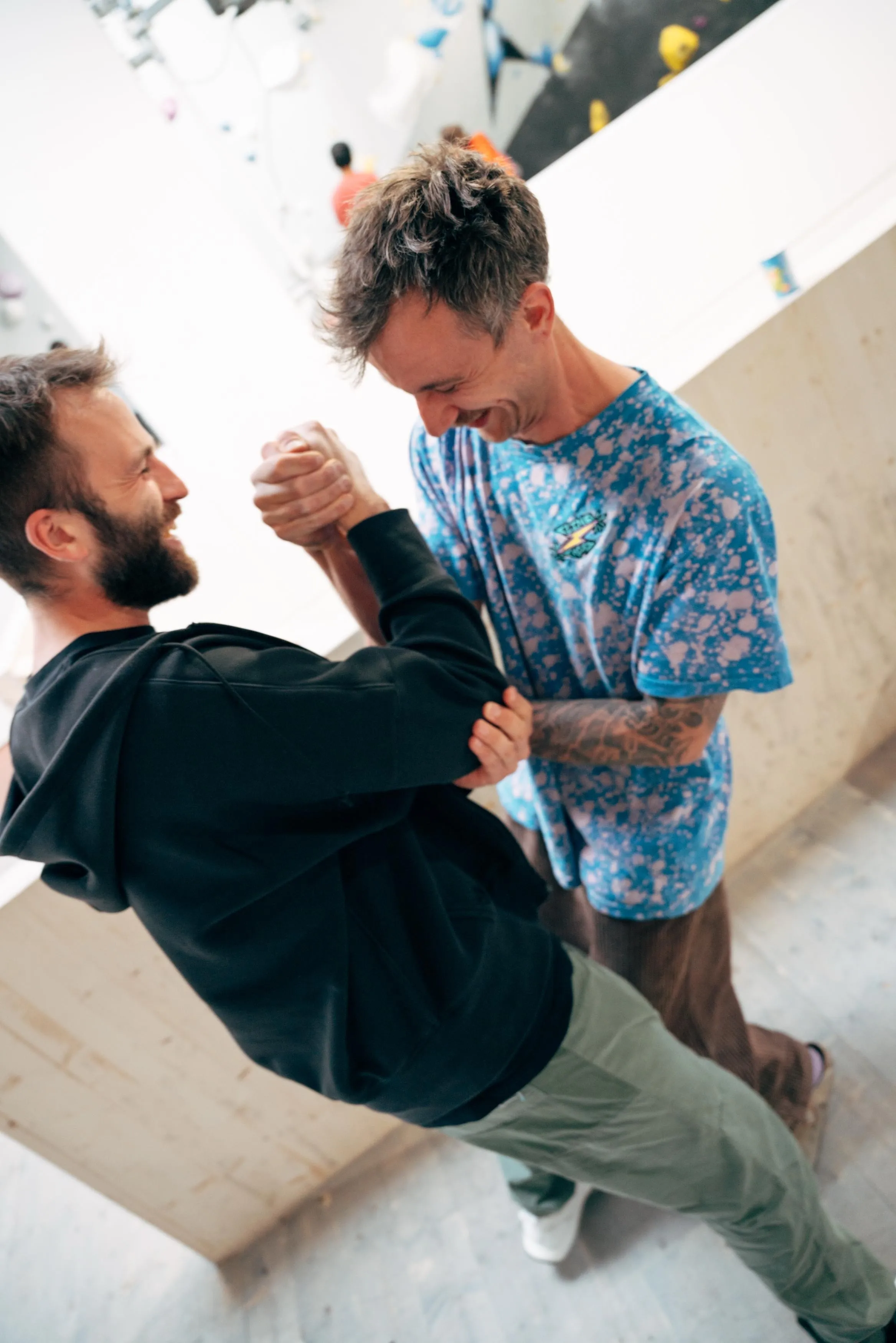Two young men engage in a playful fight, smiling, in a bright indoor setting.