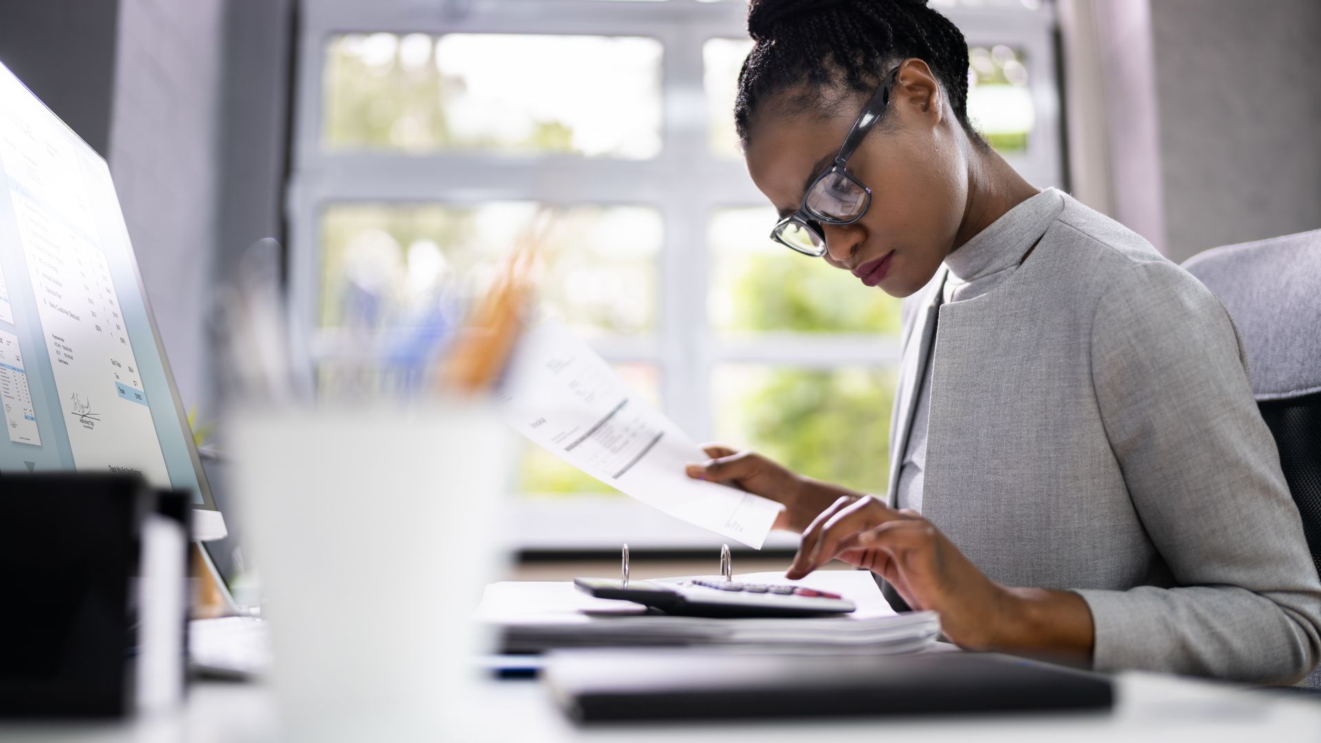 Employee in glasses reviewing printed documents at her desk