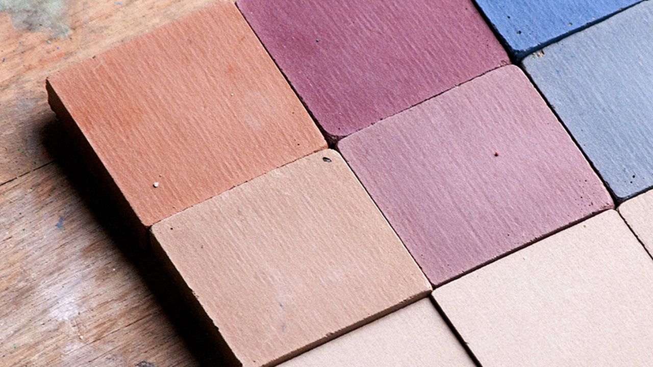 Carreaux en céramique non émaillée aux teintes naturelles terracotta, rose poudré, mauve et bleu, posés sur une surface en bois, illustrant une palette de coloris à base de pigments naturels