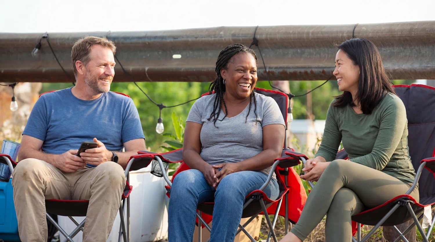 Three people sitting together outdoors and talking during a community get-together.
