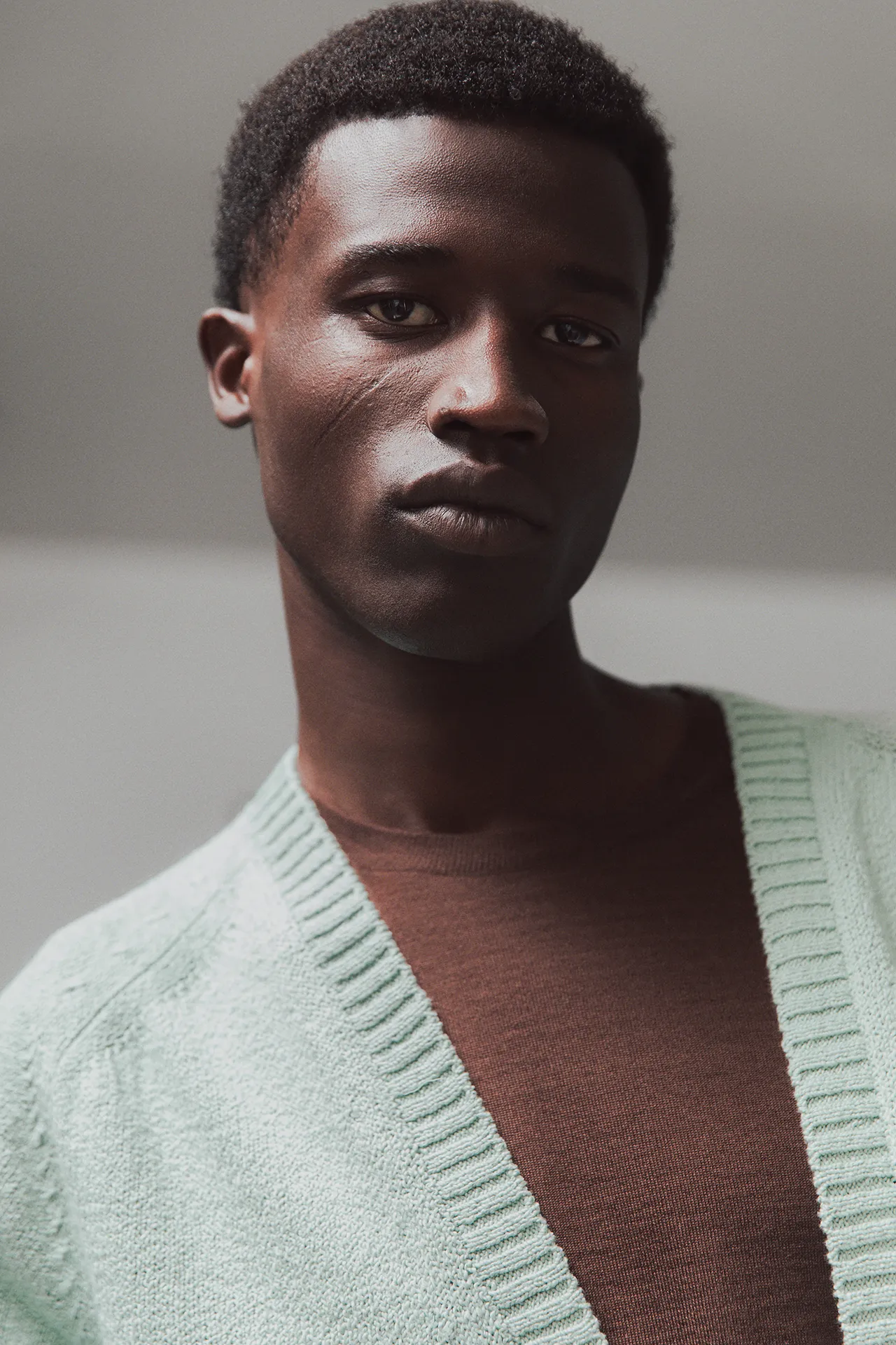 Close-up portrait of a model wearing an Aida Barni SS26 collection mint green knit cardigan with ribbed edges, layered over a brown top.
