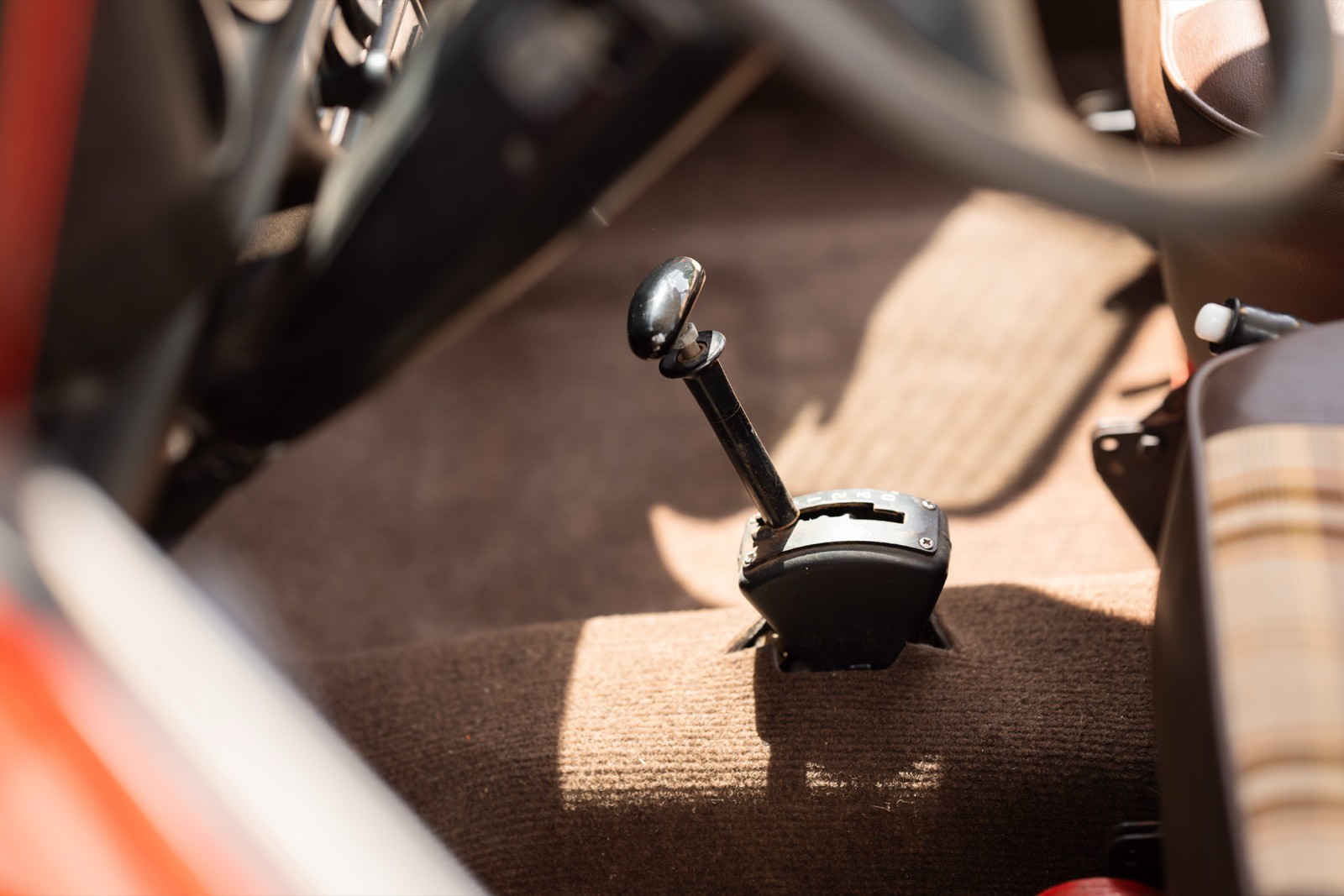 Close-up of a car's interior showing a gear shift and floor mat with sunlight casting a shadow.