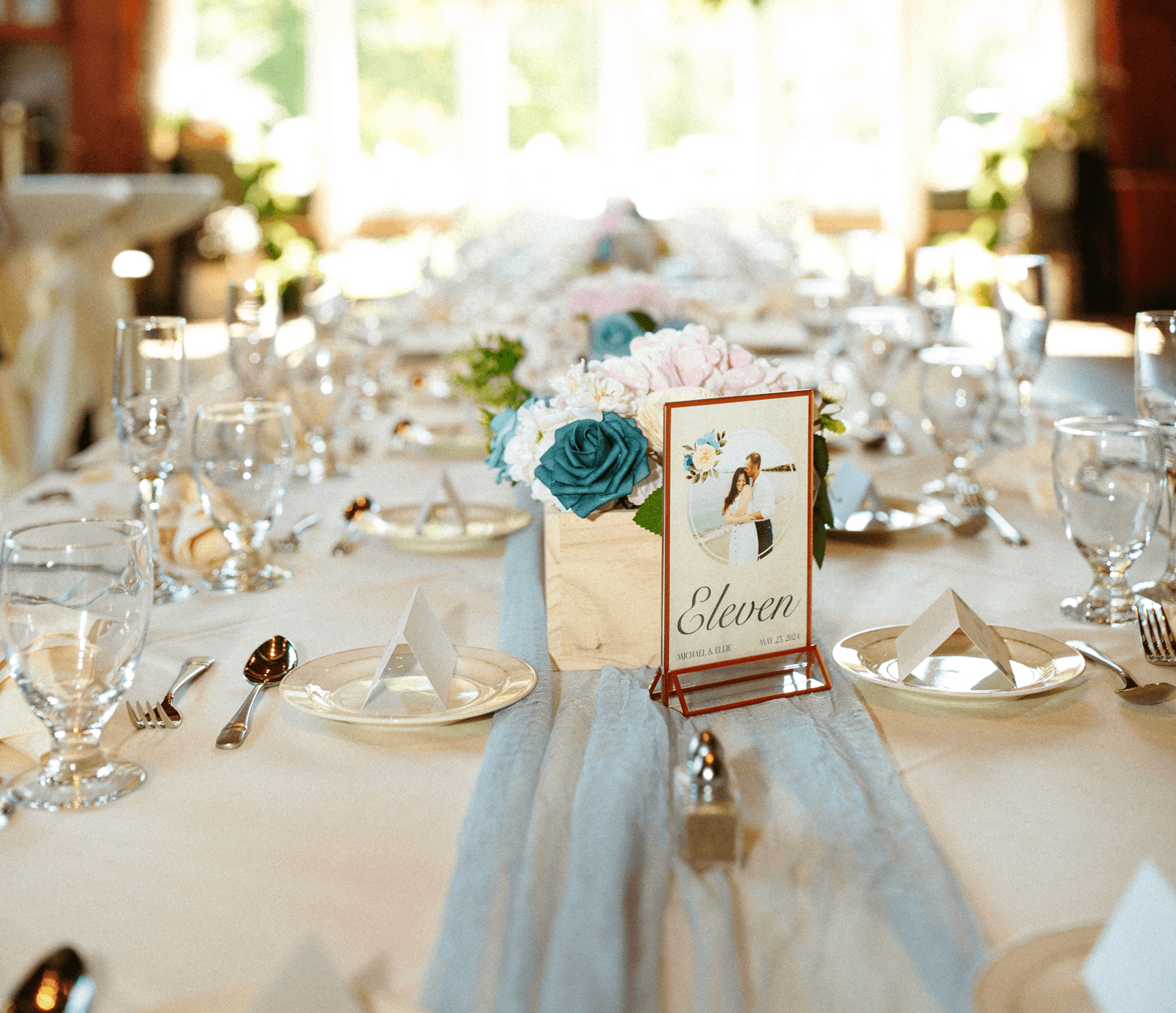 Photo of a wedding table sign designed in an elegat style with painted roses and an elegant serif typography. Designed by Will Lefkovich