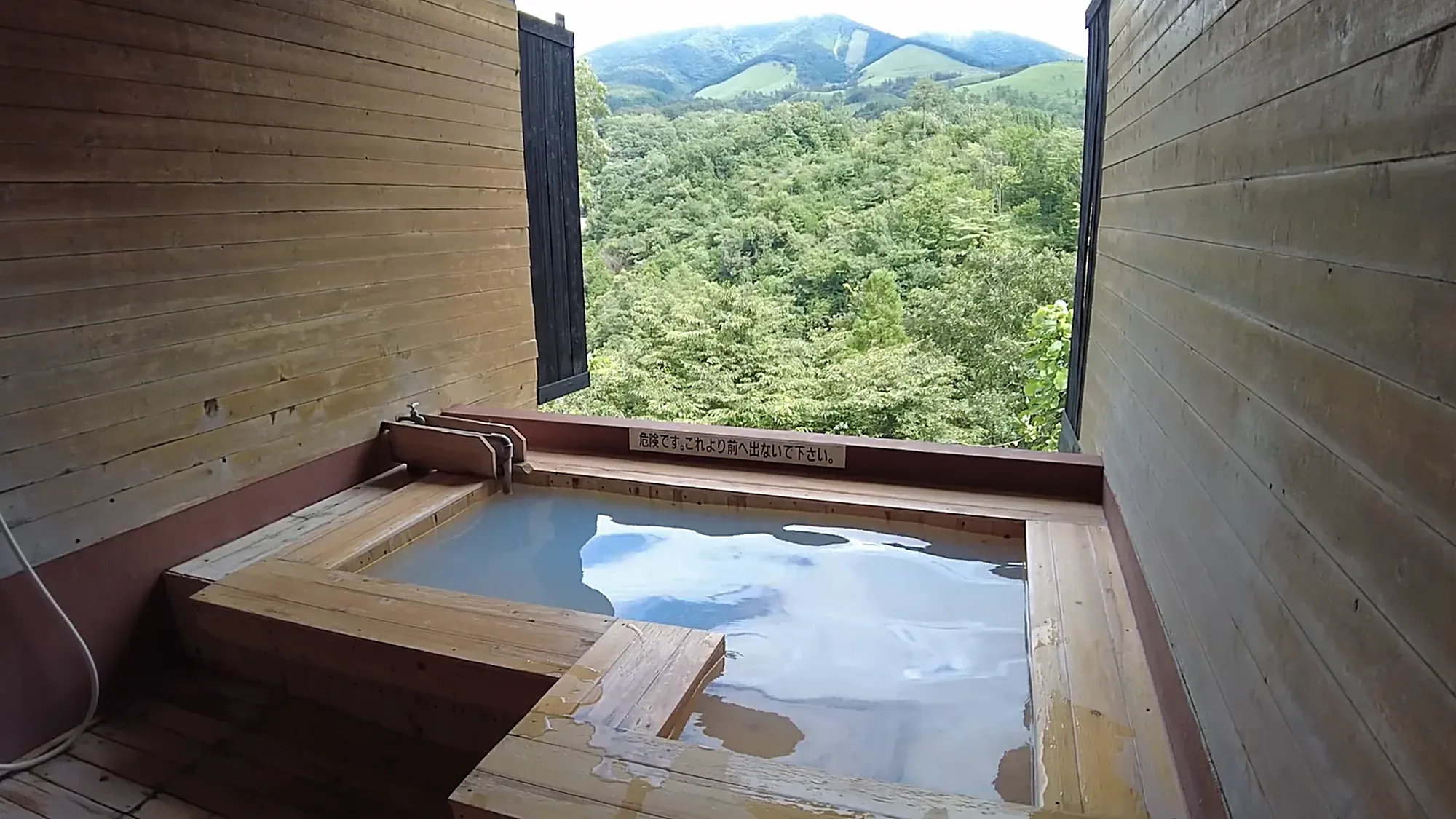 A square bath set into a concrete terrace at Kurokawa Onsen, hills beyond