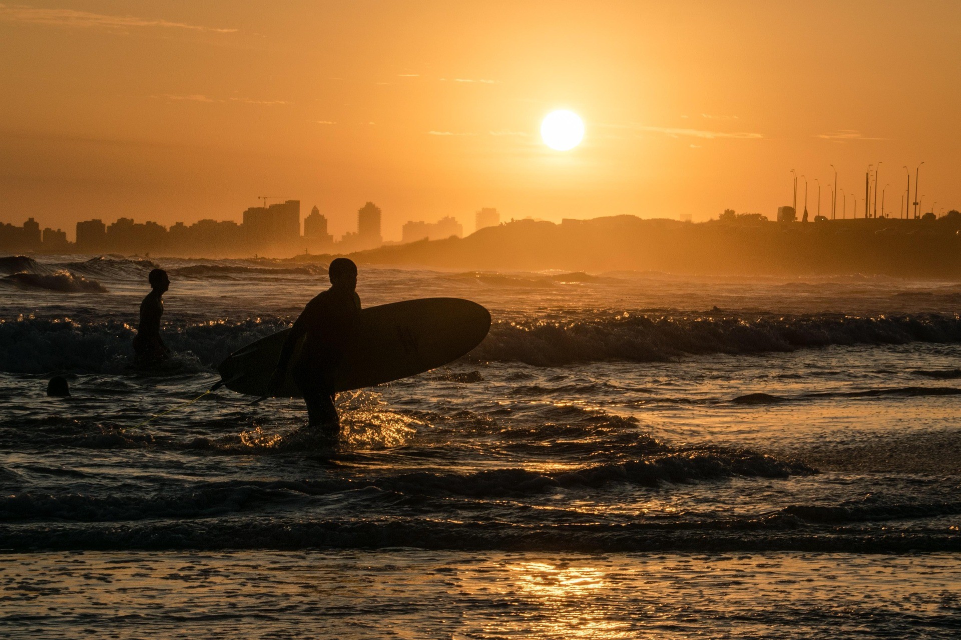 Surfista entrando al mar al atardecer en la costa de Uruguay, experiencia de playa descubierta con una aplicación de turismo con IA