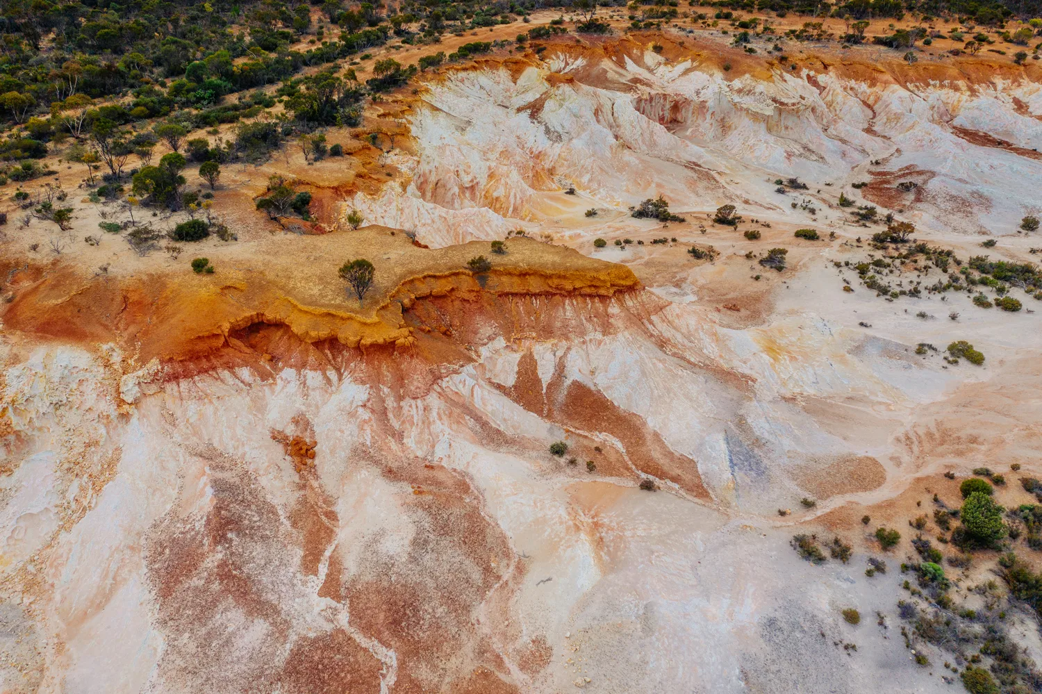 Aerial of eroded pale clay breakaways with ochre bands and low scrub