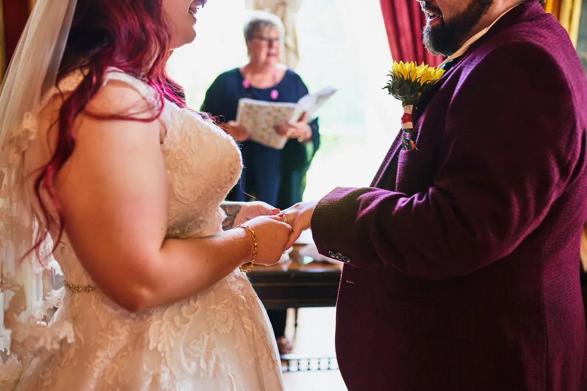 Bride and groom holding hands during their vows as the registrar reads