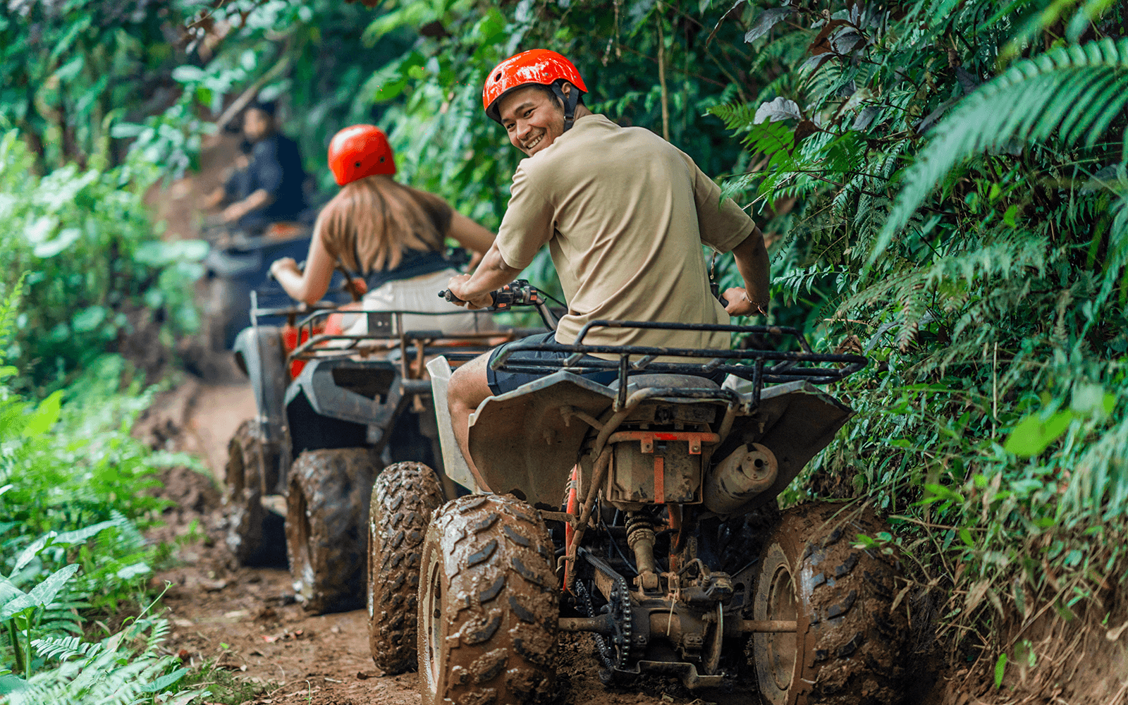 ชายยิ้มขณะขับรถเอทีวีย้อนผ่านเส้นทางป่าเขียวเข้ม.