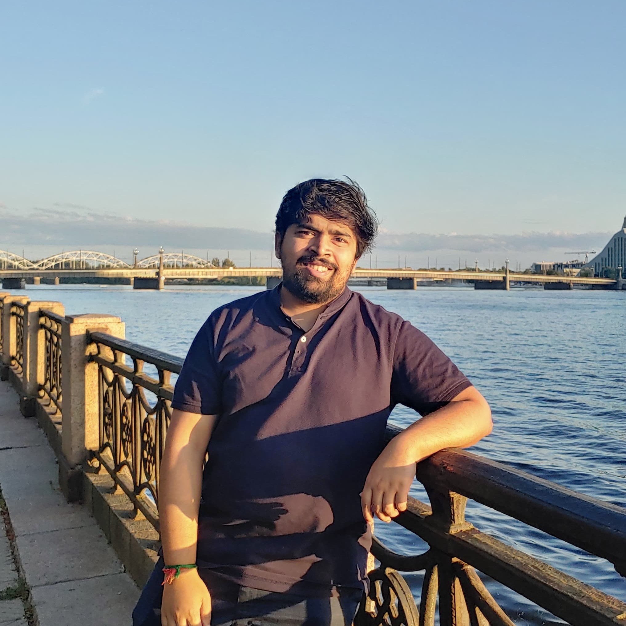 Picture of myself standing by a river leaning on a rail, smiling at the camera