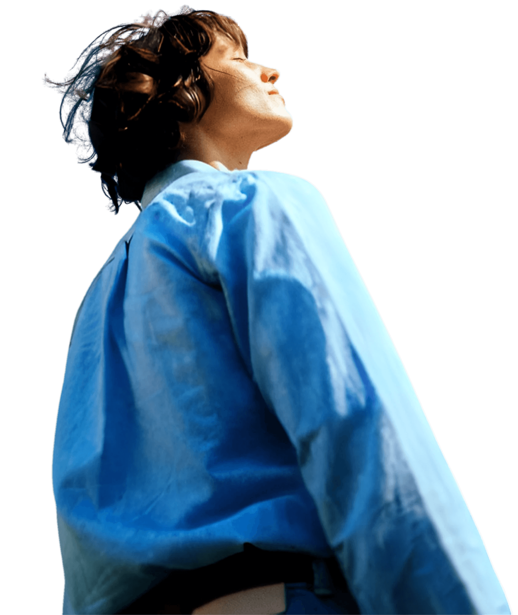 A young person with curly hair smiles at the camera while sitting in front of a laptop against a dark background.