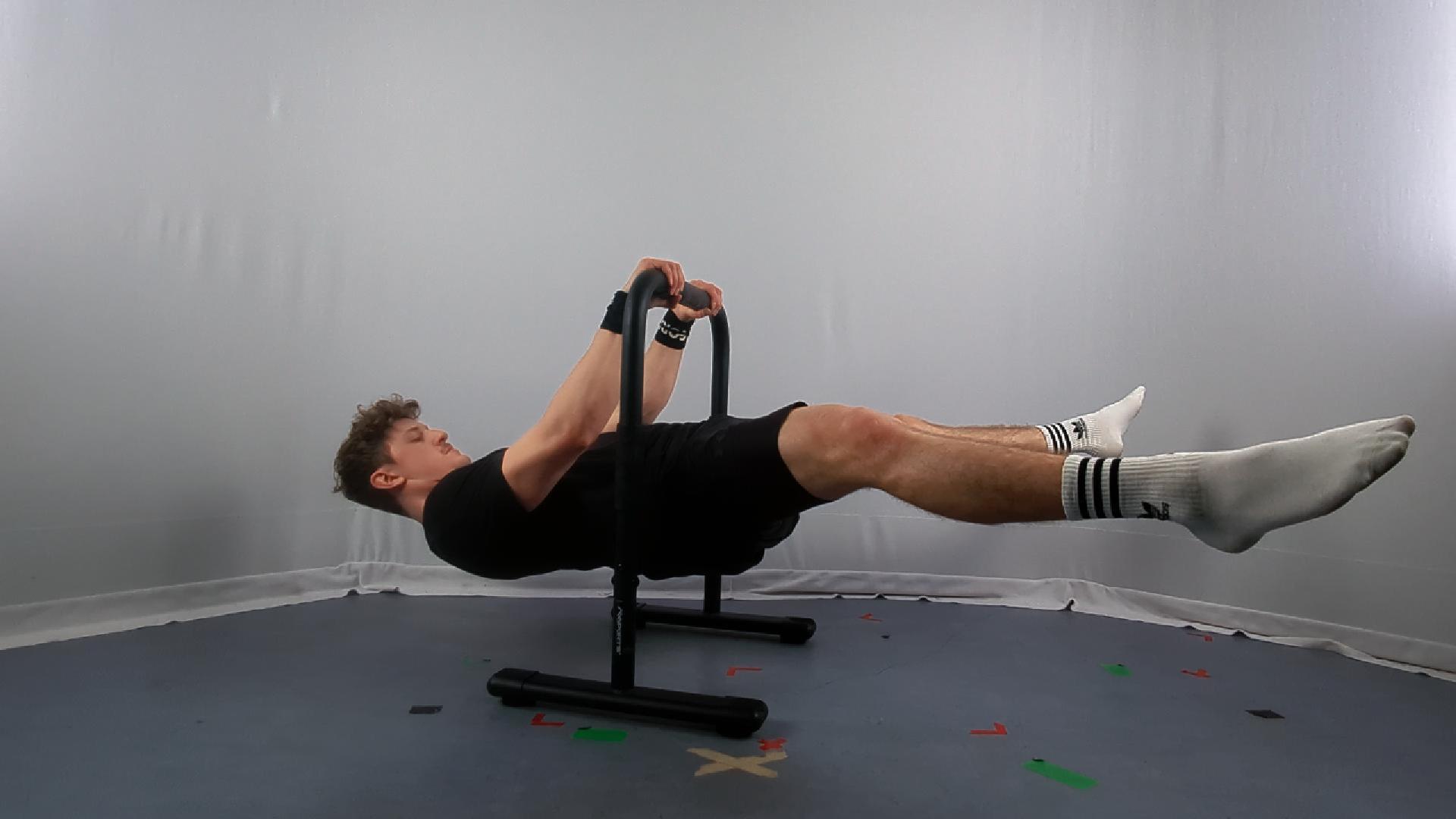 A man performs a Calisthenics Straddle Front Lever hold on parallel bars, showcasing strength and balance in a minimalist indoor setting.