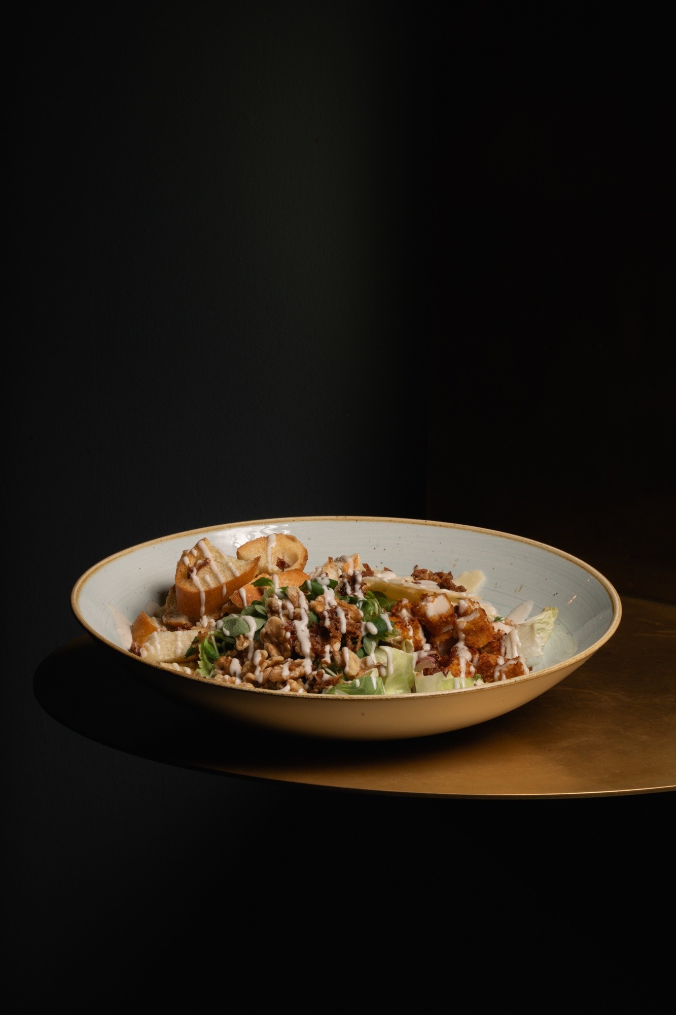 Insalata con pollo, grana, noci, crostini e salsa in superficie in ciotola bianca su sfondo scuro