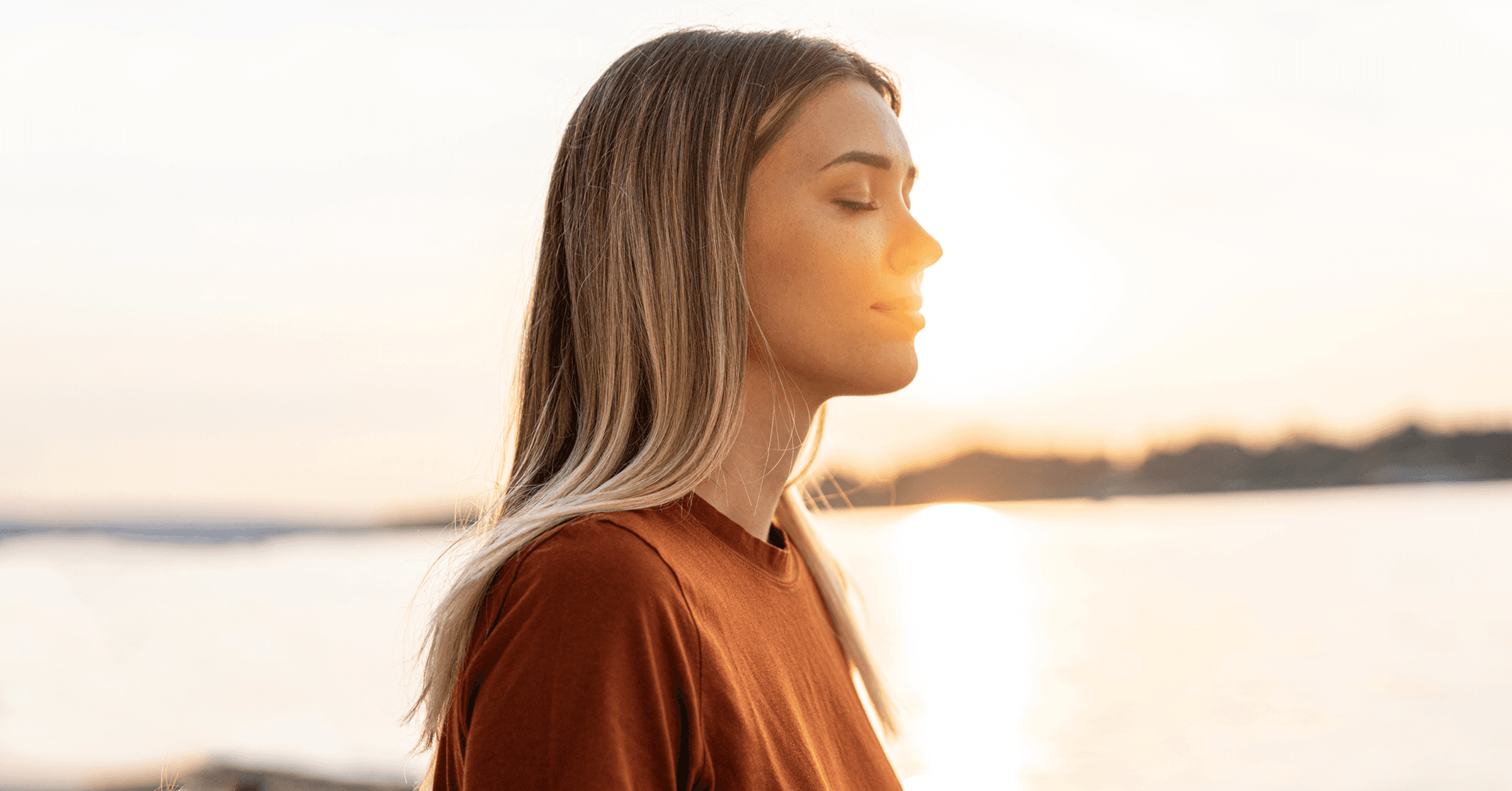En kvinna stänger sina ögon och njuter av tystnaden vid vattnet vid soluppgången.