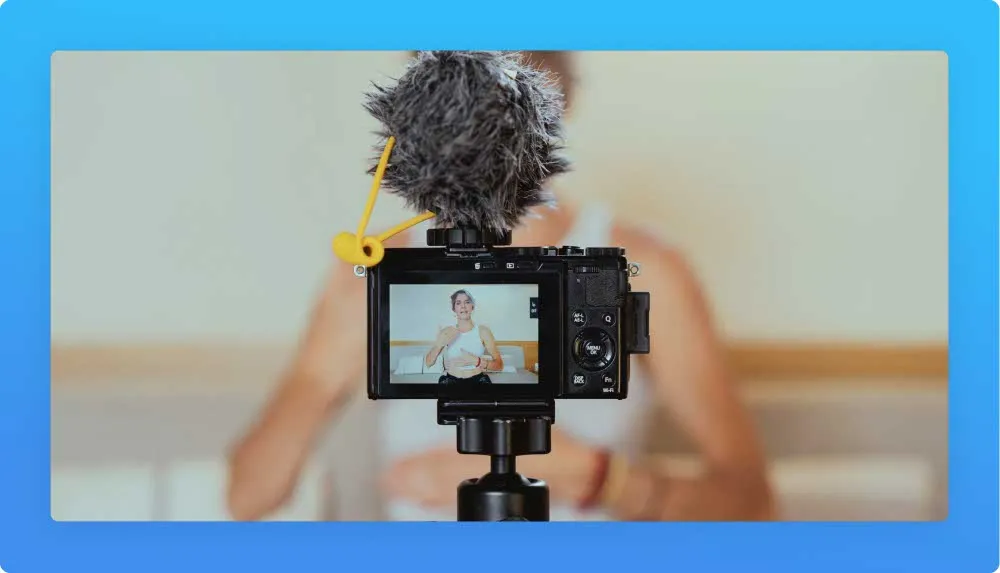 Close view of a camera with a wind muff microphone recording a woman talking. Blured image of the woman in the background