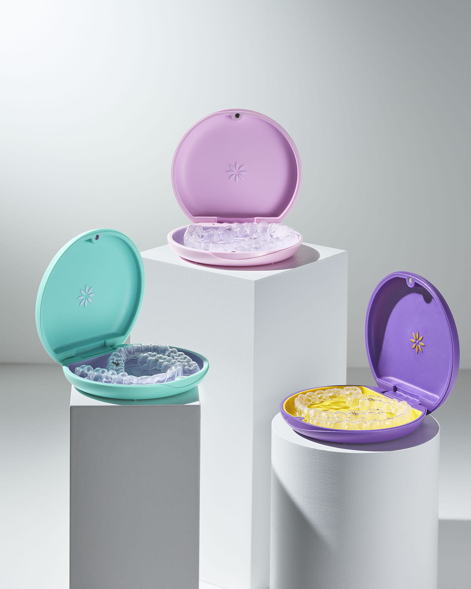 Colorful orthodontic retainer cases with aligners on white pedestals.