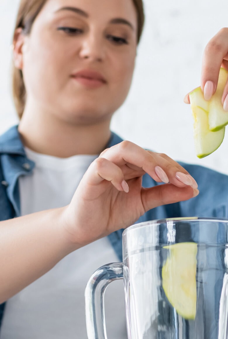 A woman placing apples in a blender.